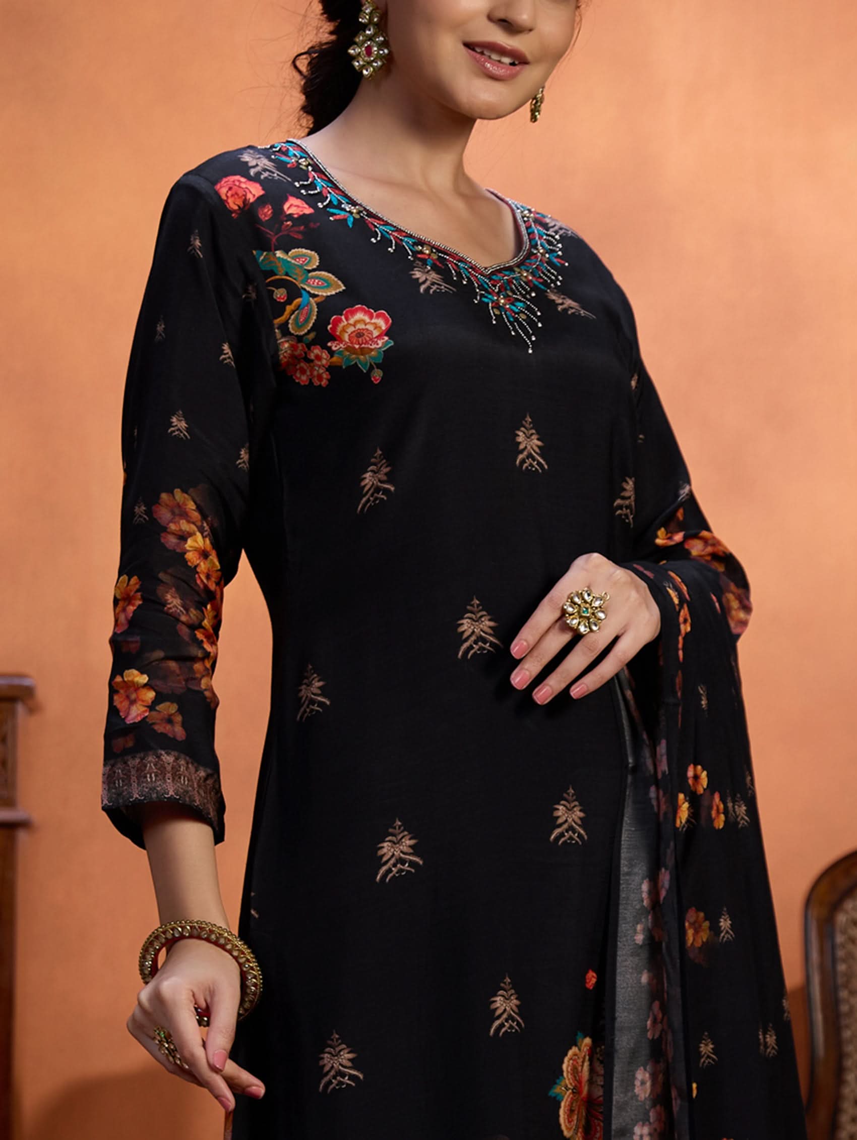 Woman wearing a black embroidered outfit with colorful patterns on an orange background