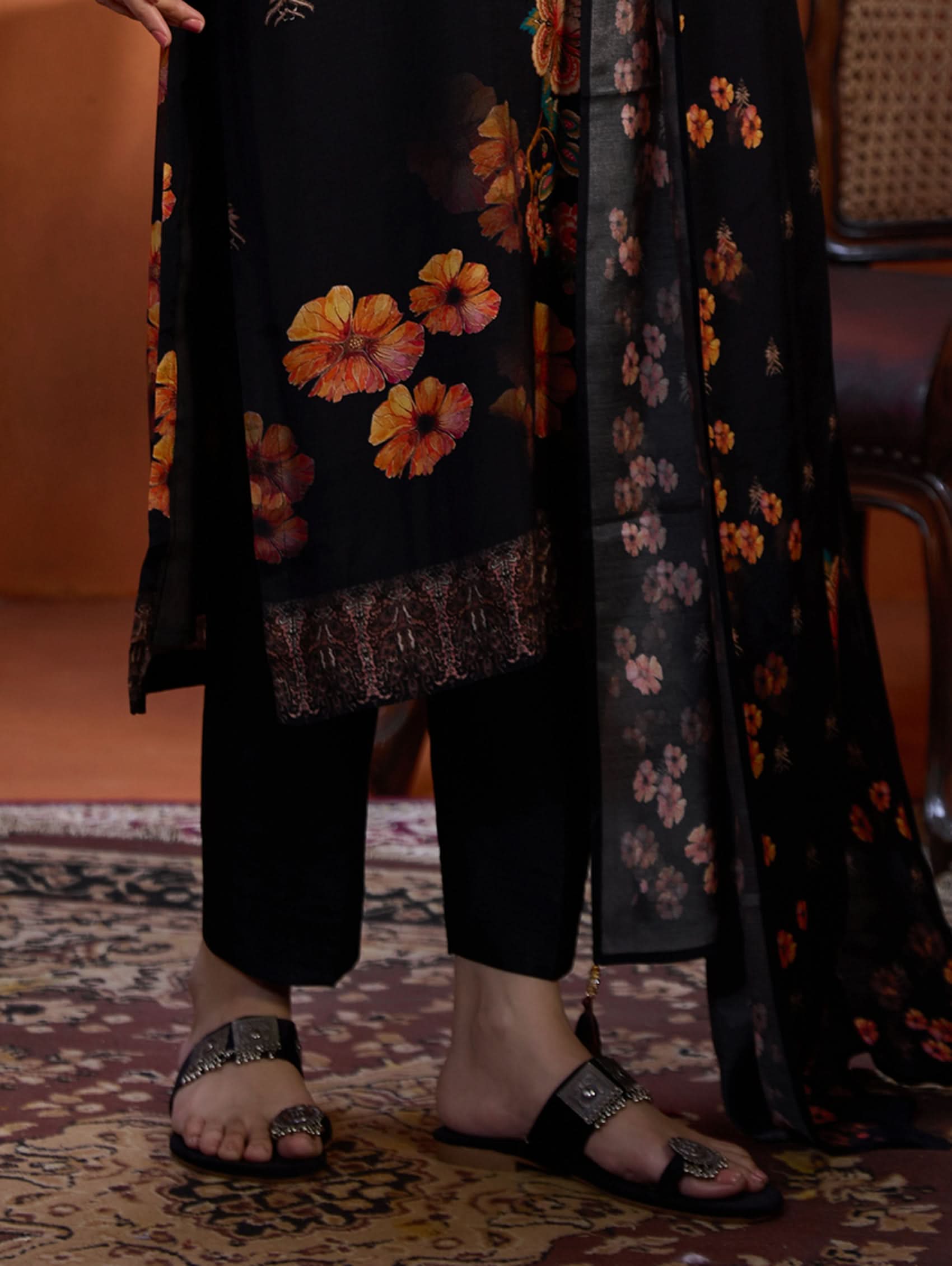 Person wearing a floral outfit with black pants and sandals on a patterned rug.