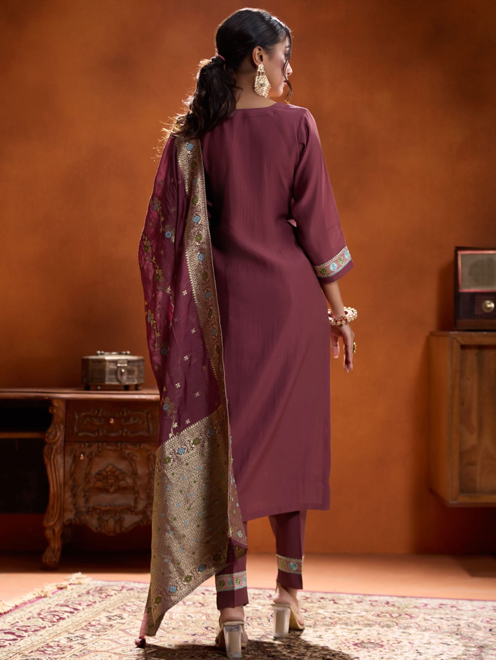A woman modeling a maroon embroidered viscose silk suit set with a round neckline, three-fourth sleeves, and a dupatta. The set features cording thread embroidery along with hand embroidery.
