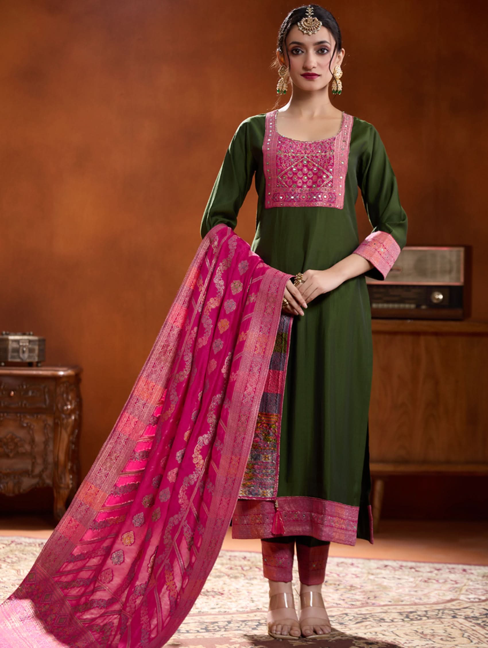 A woman modeling a green embroidered viscose silk suit set with a dupatta, featuring hand embroidery on the meenakari-jacquard weave silk yoke.