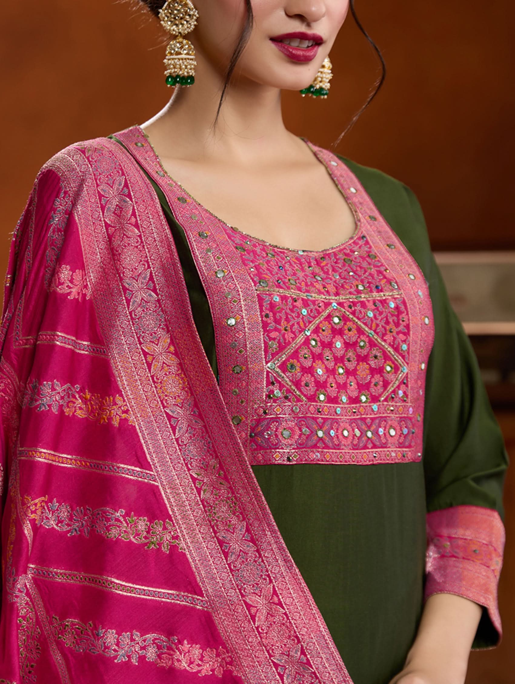 A woman modeling a green embroidered viscose silk suit set with a dupatta, featuring hand embroidery on the meenakari-jacquard weave silk yoke.