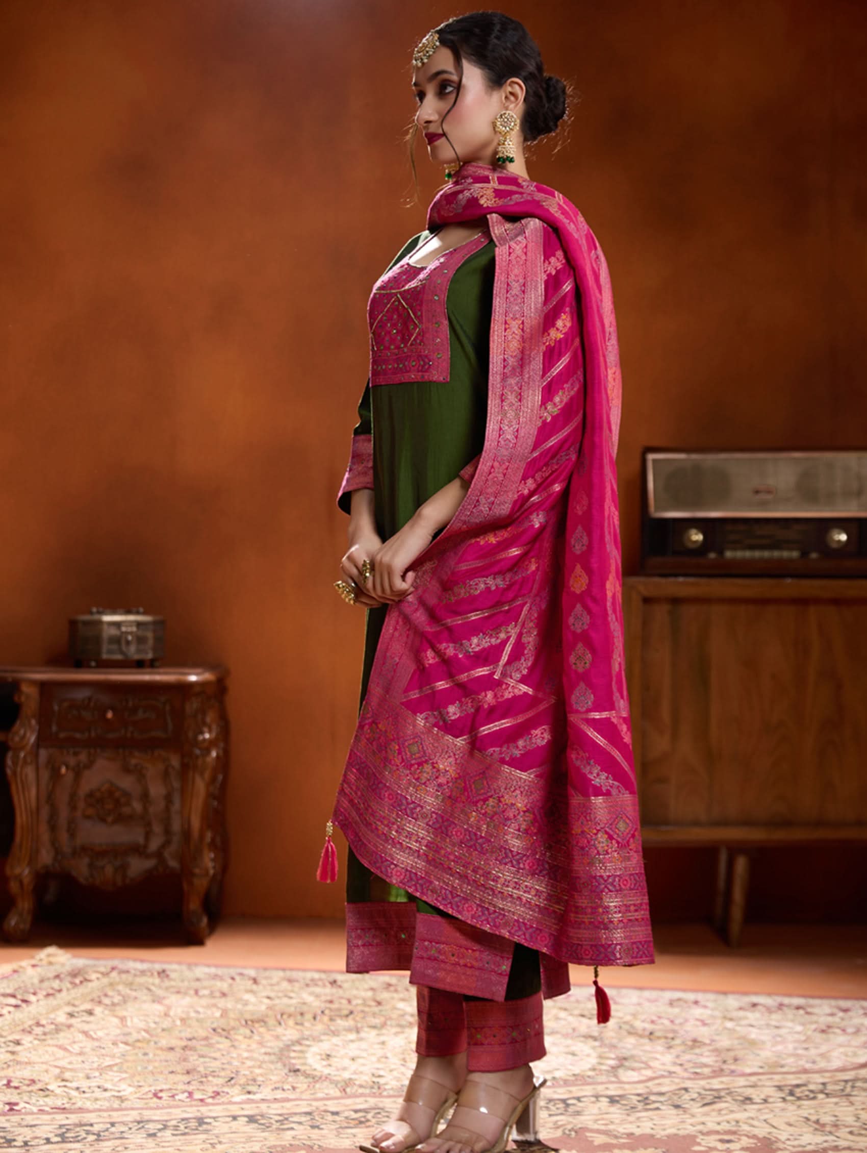 A woman modeling a green embroidered viscose silk suit set with a dupatta, featuring hand embroidery on the meenakari-jacquard weave silk yoke.