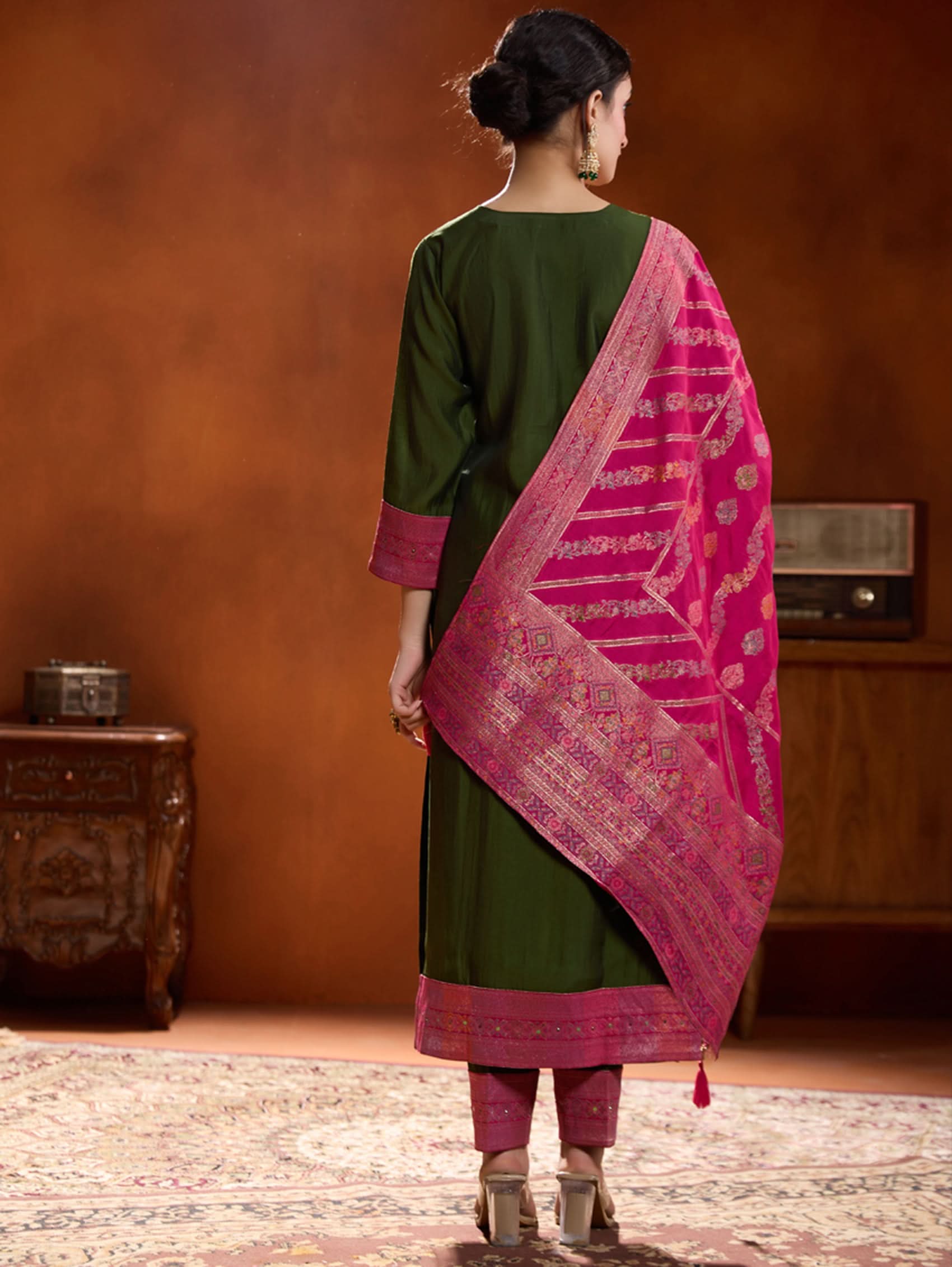 A woman modeling a green embroidered viscose silk suit set with a dupatta, featuring hand embroidery on the meenakari-jacquard weave silk yoke.