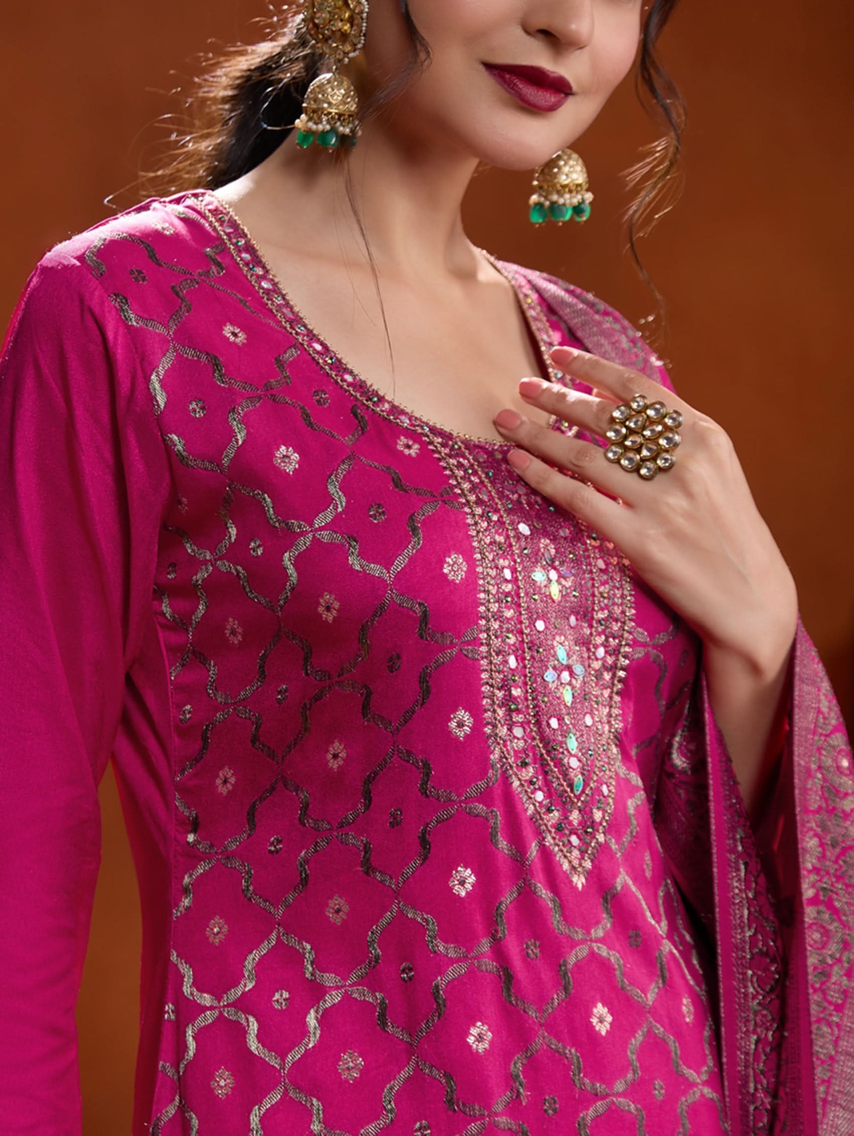 A woman wearing a pink jacquard weave silk suit set with hand-embroidered details, consisting of a kurta with three-fourth sleeves, a round neckline, and side slits, paired with pants and a dupatta.