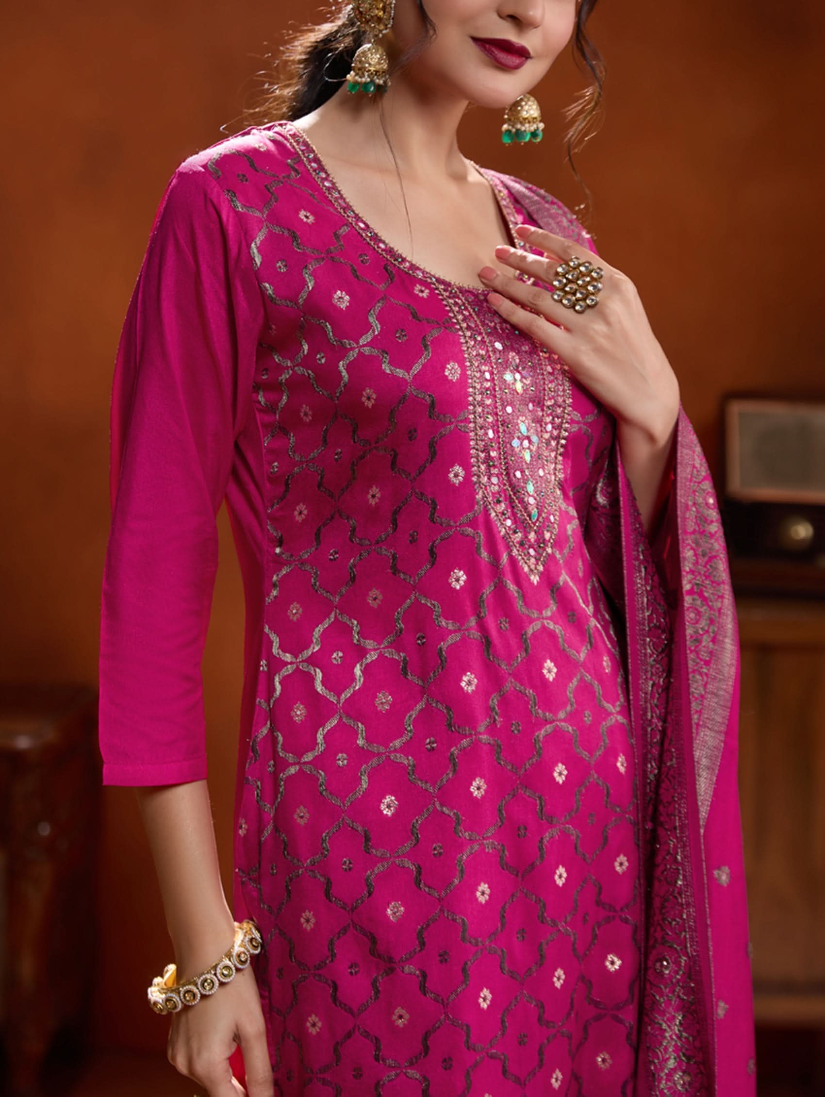 A woman wearing a pink jacquard weave silk suit set with hand-embroidered details, consisting of a kurta with three-fourth sleeves, a round neckline, and side slits, paired with pants and a dupatta.