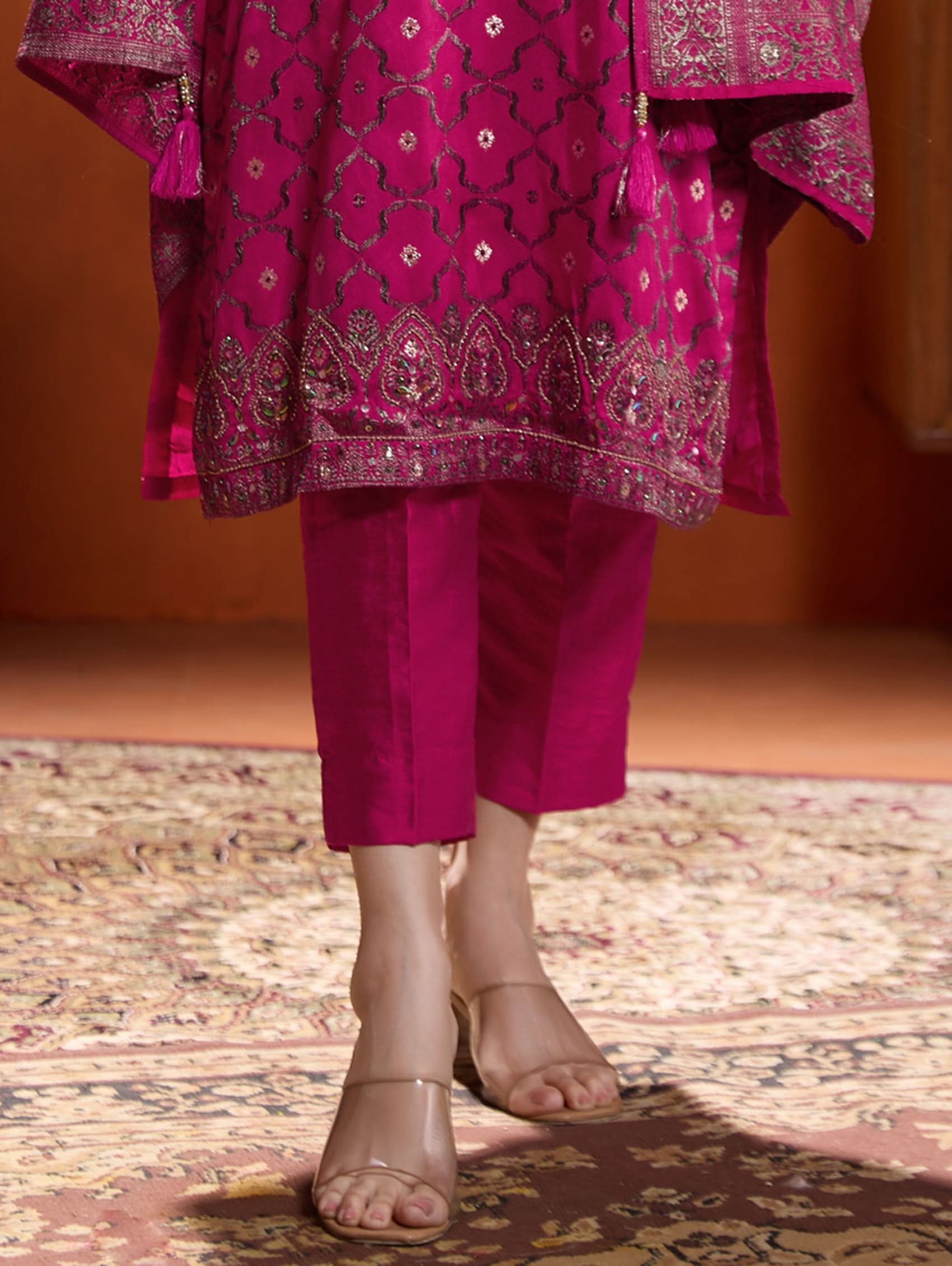 A woman wearing a pink jacquard weave silk suit set with hand-embroidered details, consisting of a kurta with three-fourth sleeves, a round neckline, and side slits, paired with pants and a dupatta.
