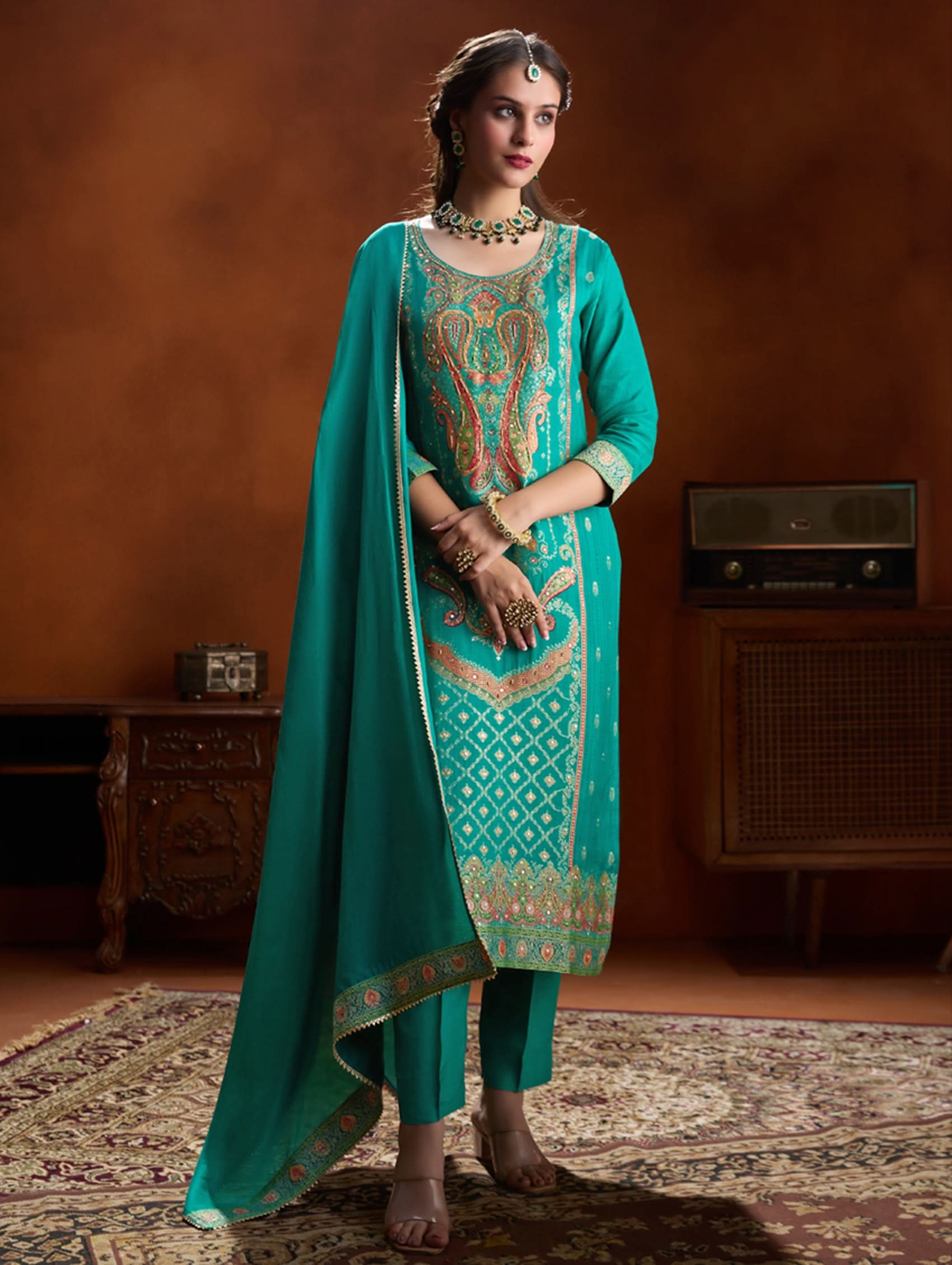 Woman in a teal traditional outfit with embroidery in a vintage room.