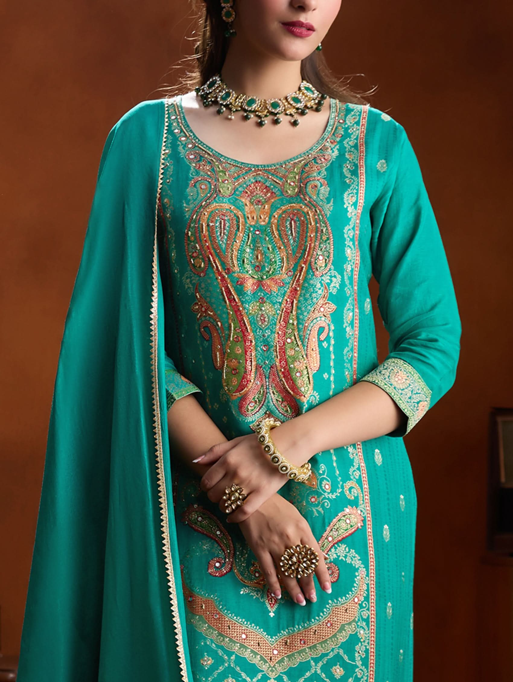 Teal embroidered traditional outfit with jewelry on a brown background