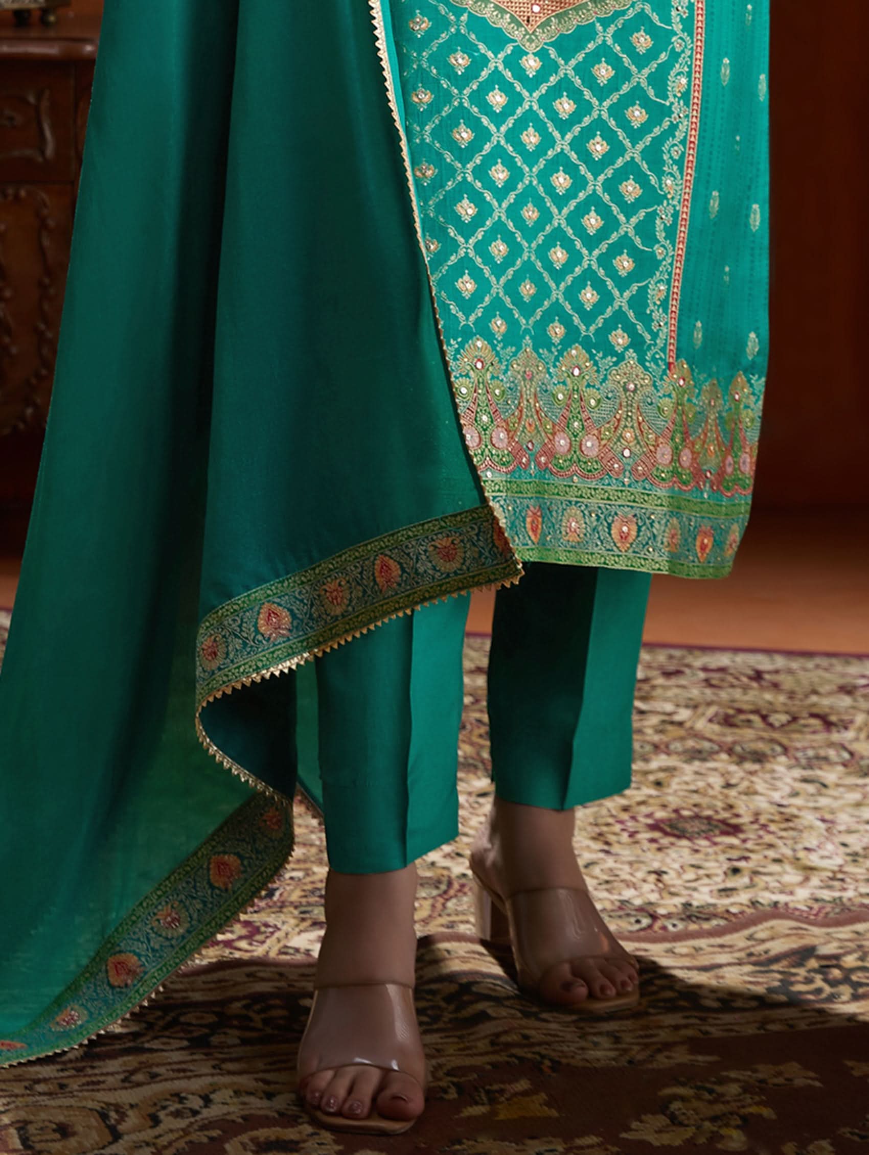 Teal traditional outfit with intricate patterns on a textured floor.