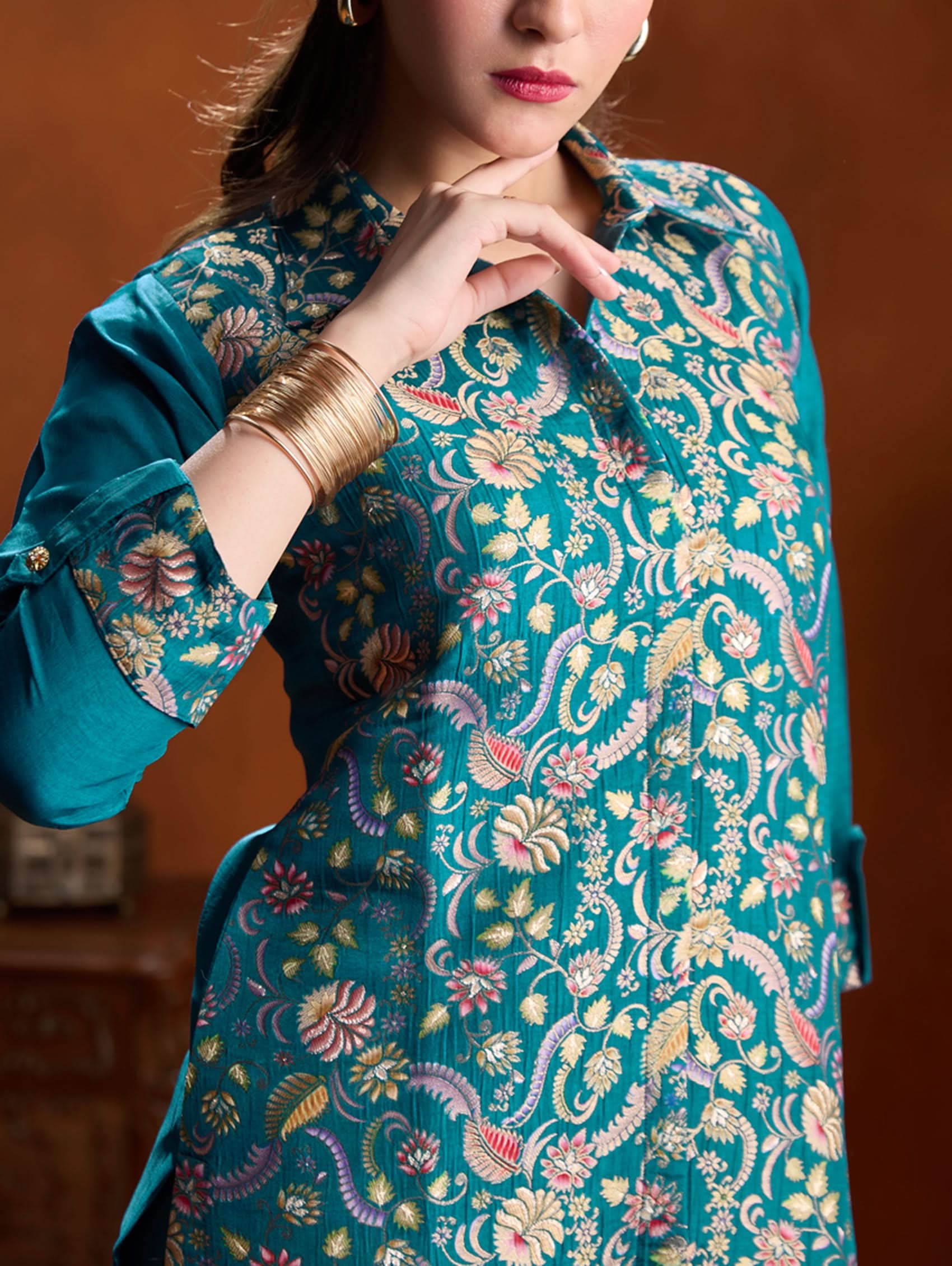 Woman wearing a teal floral patterned blouse against a brown background