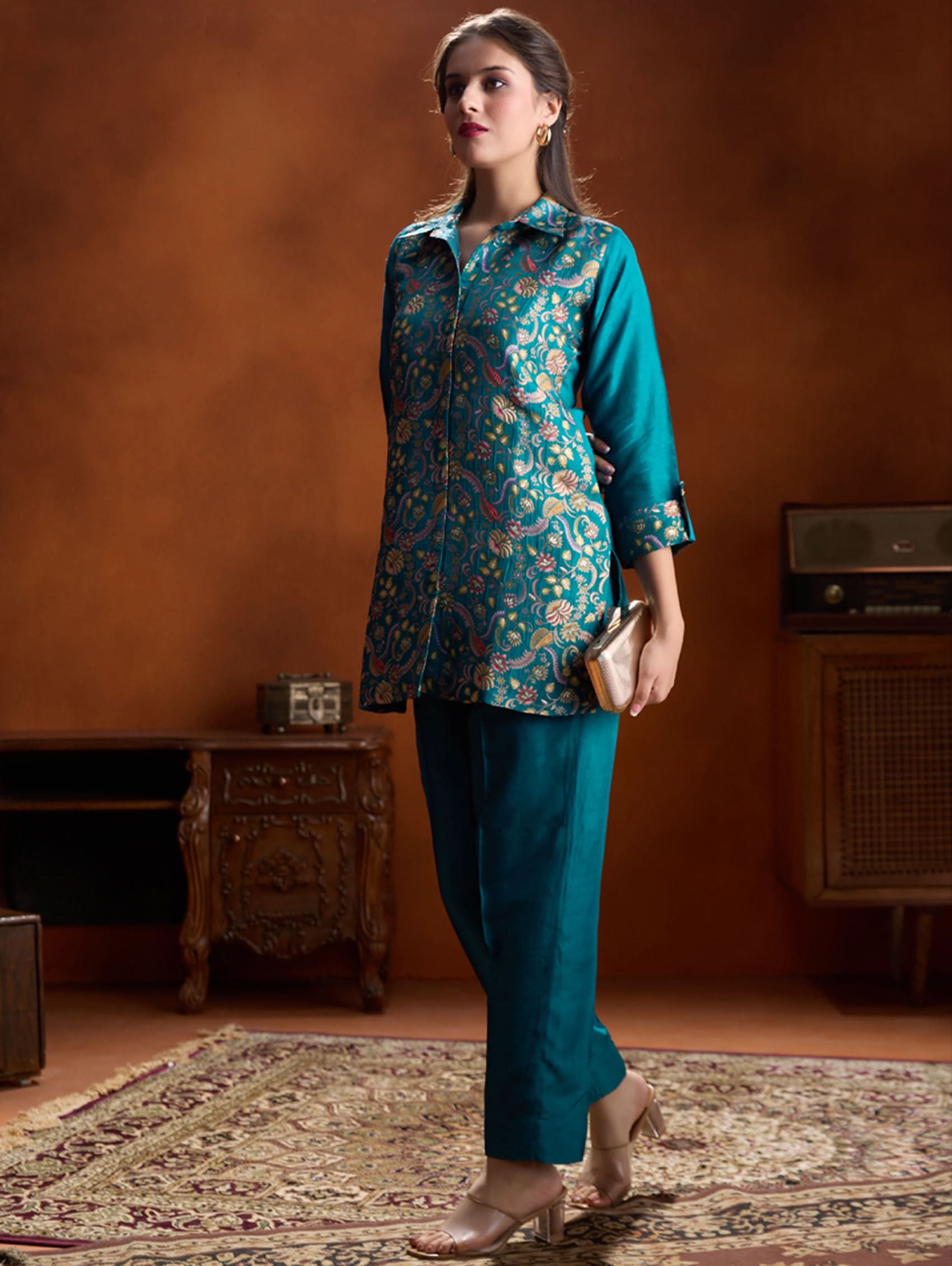Woman wearing a teal floral blouse and pants in a vintage room.
