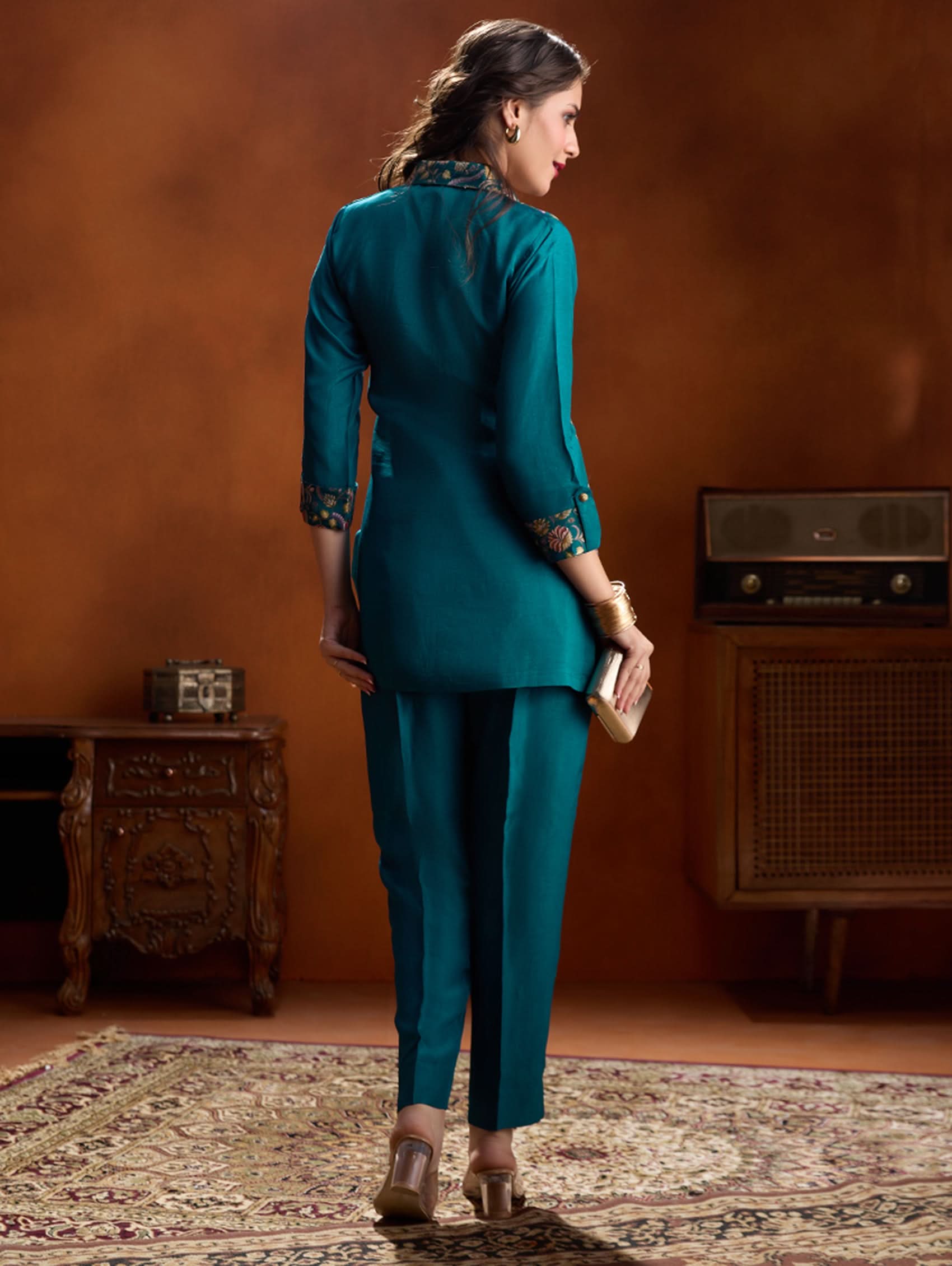 Woman in teal outfit standing in a room with vintage furniture.