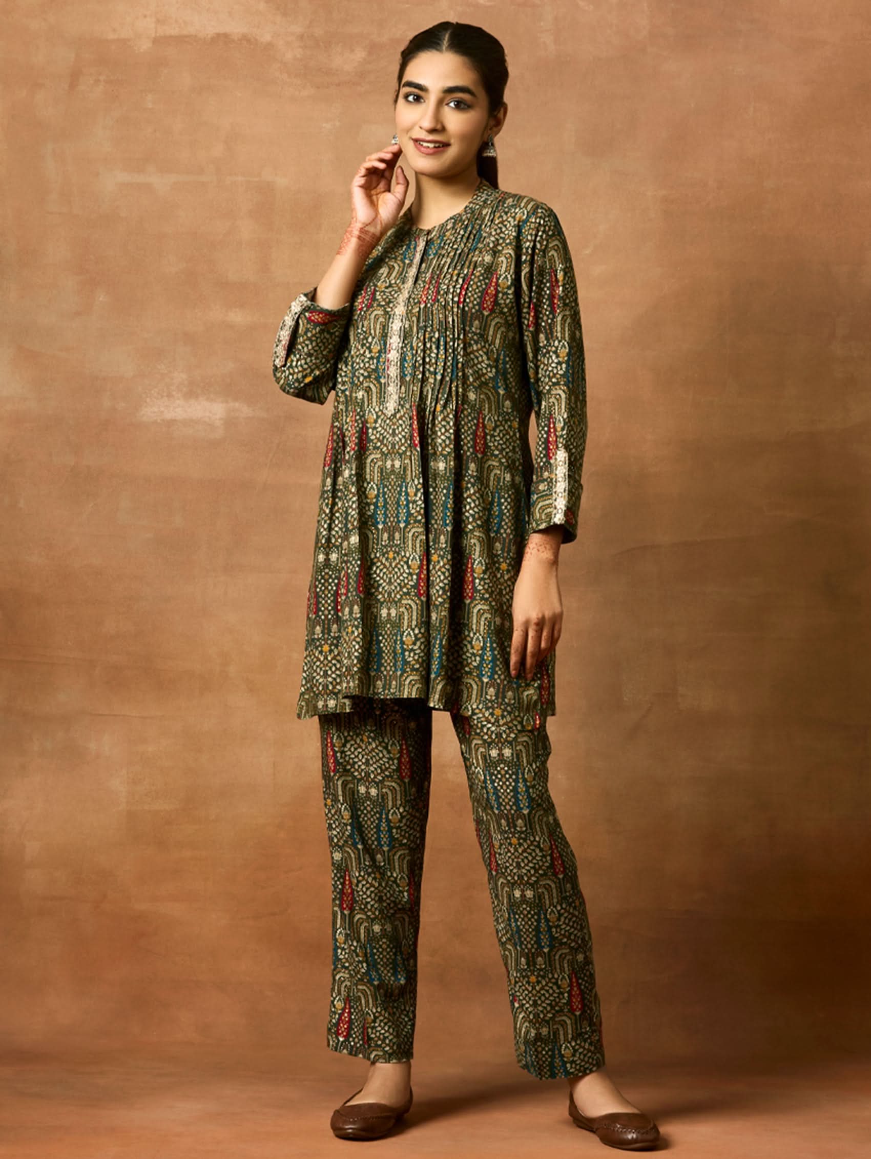A woman modeling a green and orange floral printed viscose rayon co-ord set with a mandarin collar and three-fourth sleeves kurta, and matching pants with a partially elasticated waistband and side pockets.