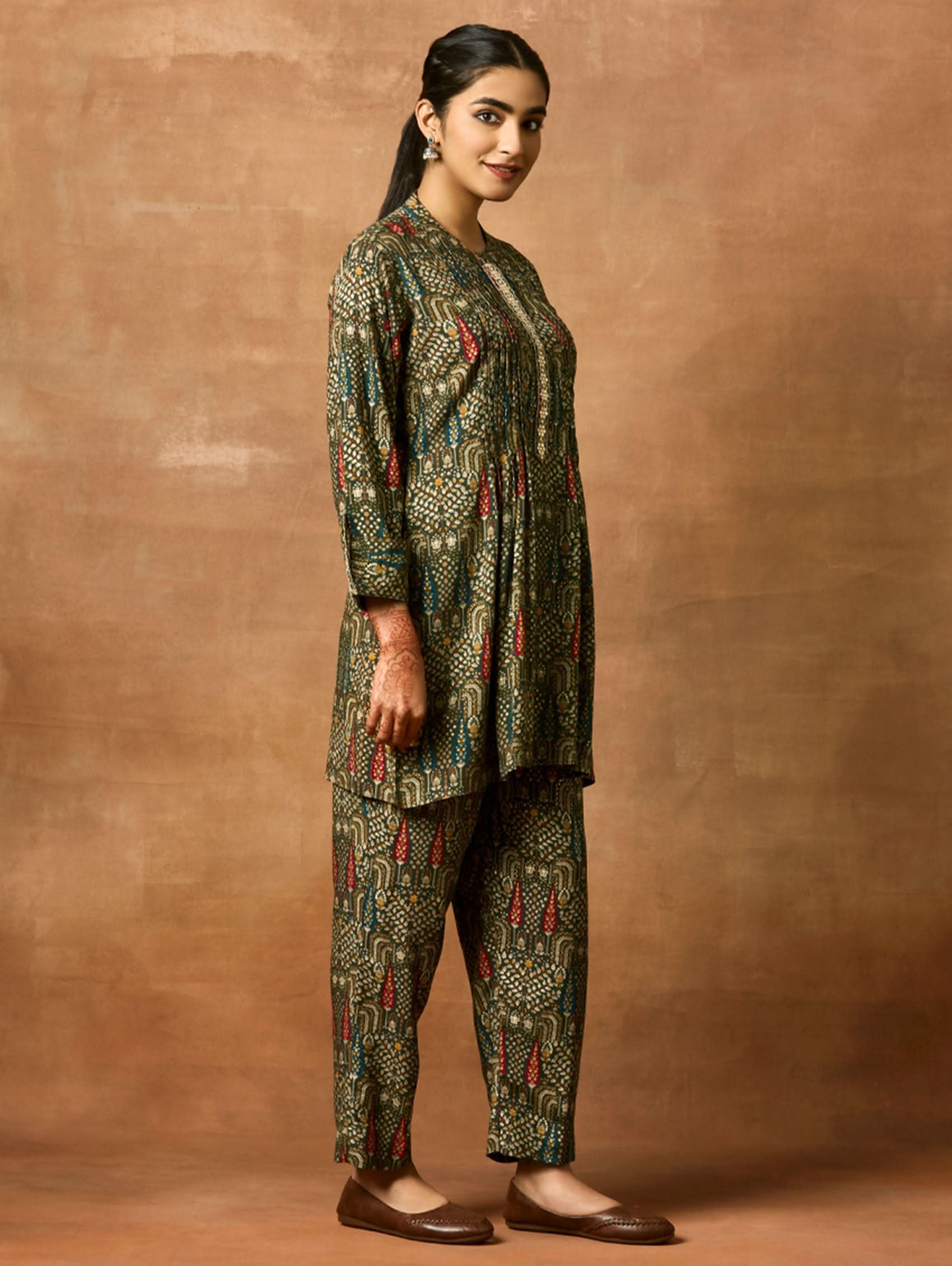A woman modeling a green and orange floral printed viscose rayon co-ord set with a mandarin collar and three-fourth sleeves kurta, and matching pants with a partially elasticated waistband and side pockets.