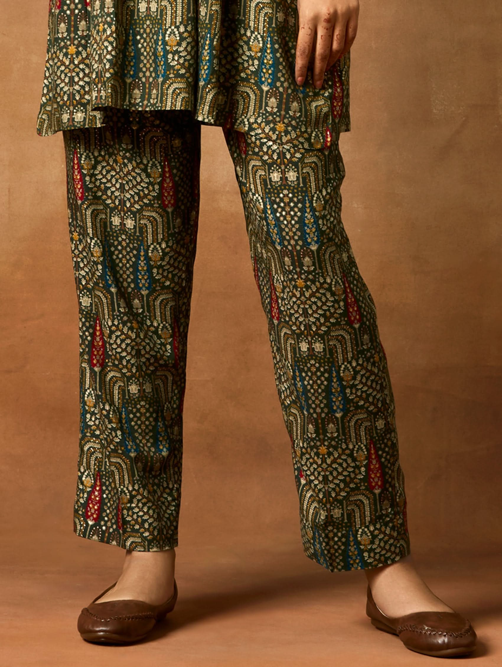 A woman modeling a green and orange floral printed viscose rayon co-ord set with a mandarin collar and three-fourth sleeves kurta, and matching pants with a partially elasticated waistband and side pockets.