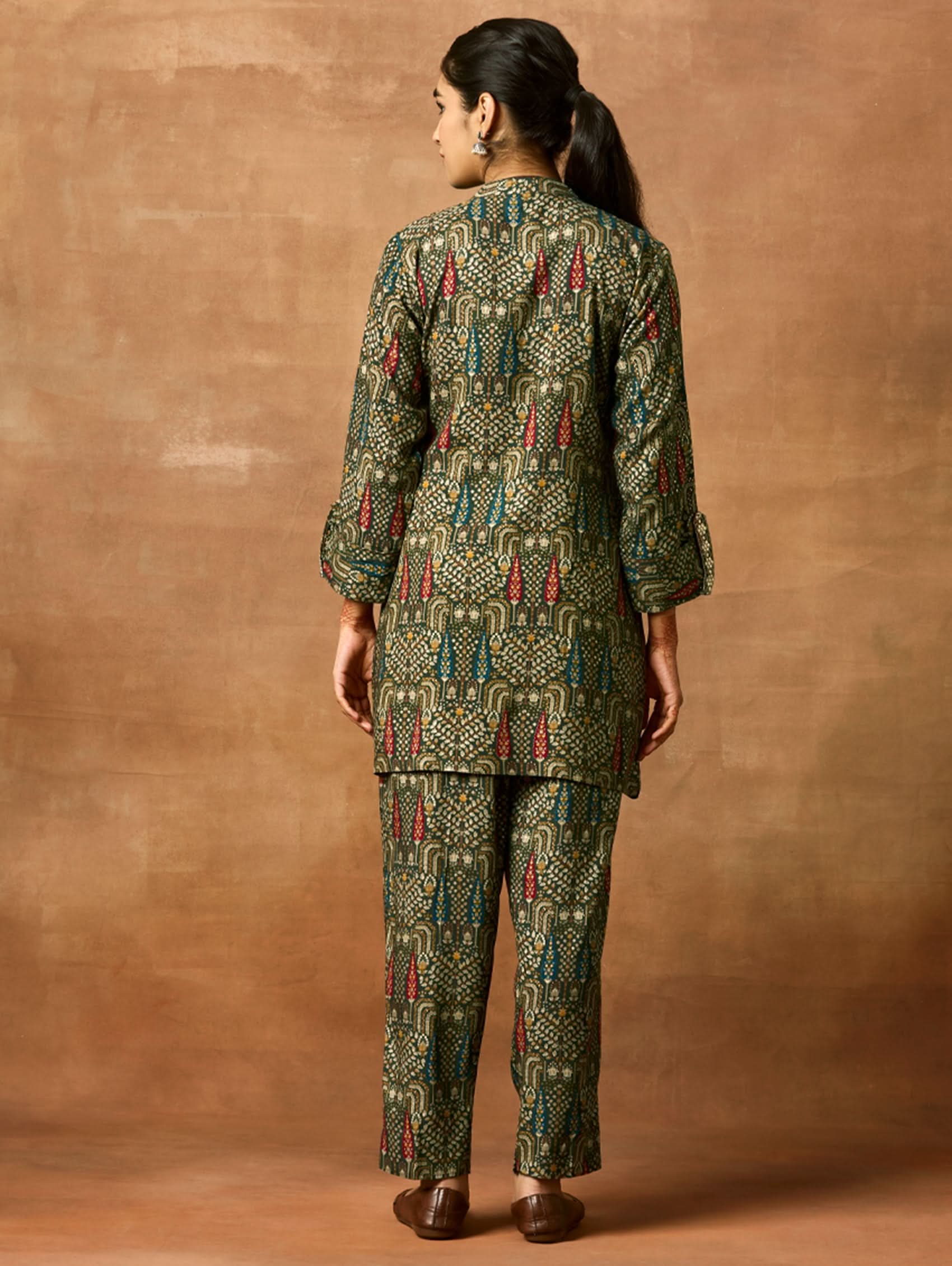 A woman modeling a green and orange floral printed viscose rayon co-ord set with a mandarin collar and three-fourth sleeves kurta, and matching pants with a partially elasticated waistband and side pockets.