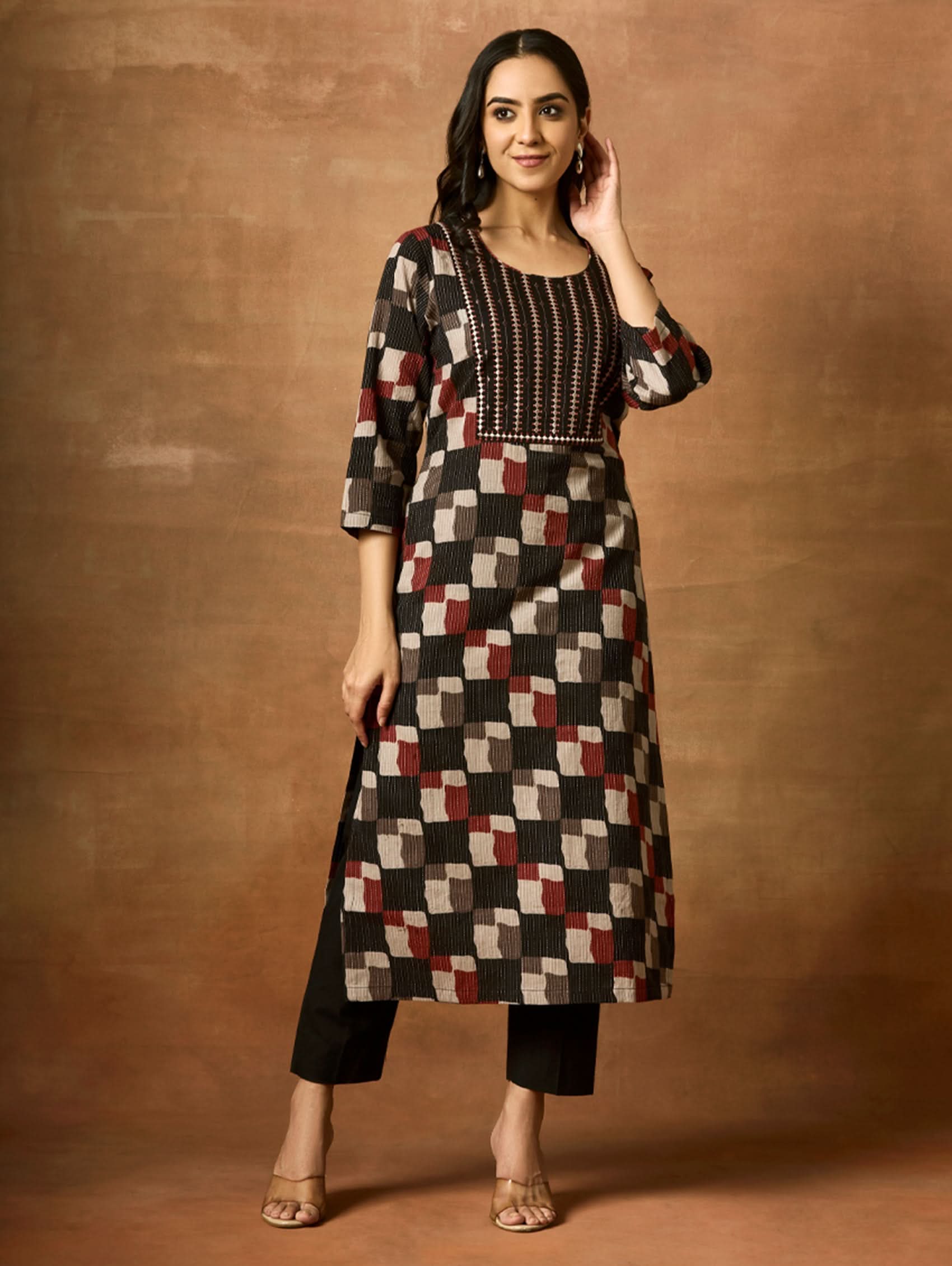 A woman wearing a geometric patterned kurta with round neckline and three-fourth sleeves, paired with trousers.
