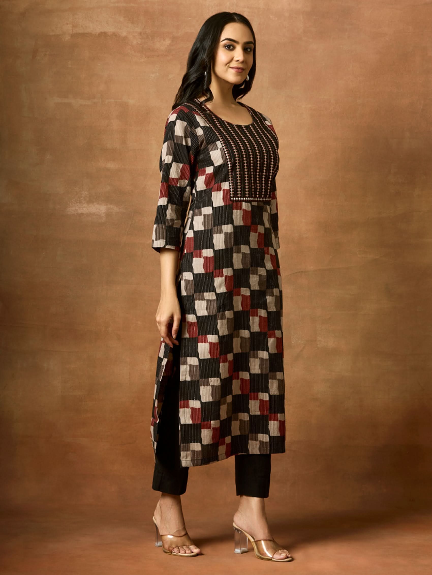 Woman wearing a patterned kurta and pants against a brown background