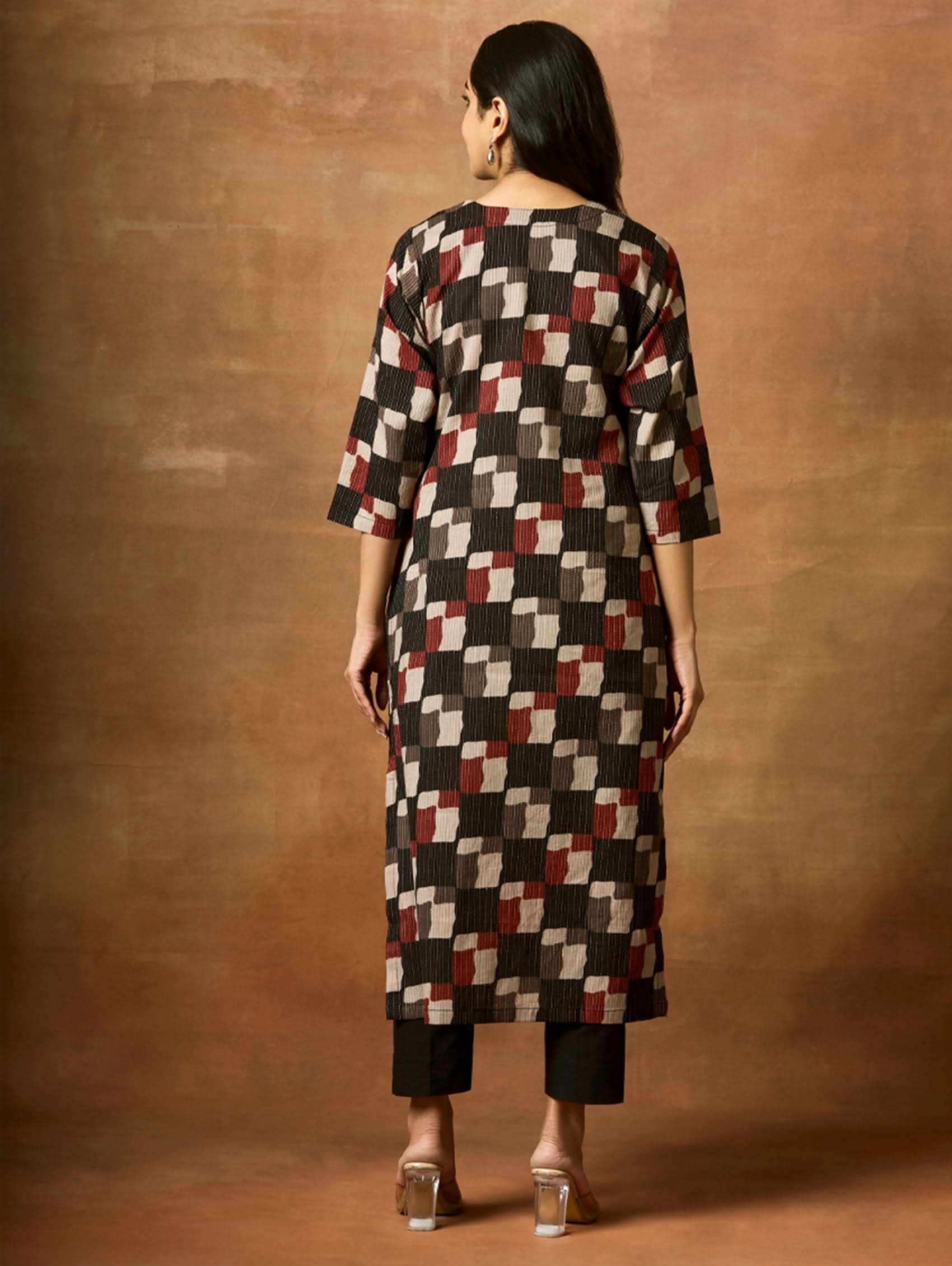 Person wearing a patterned kurta against a brown background