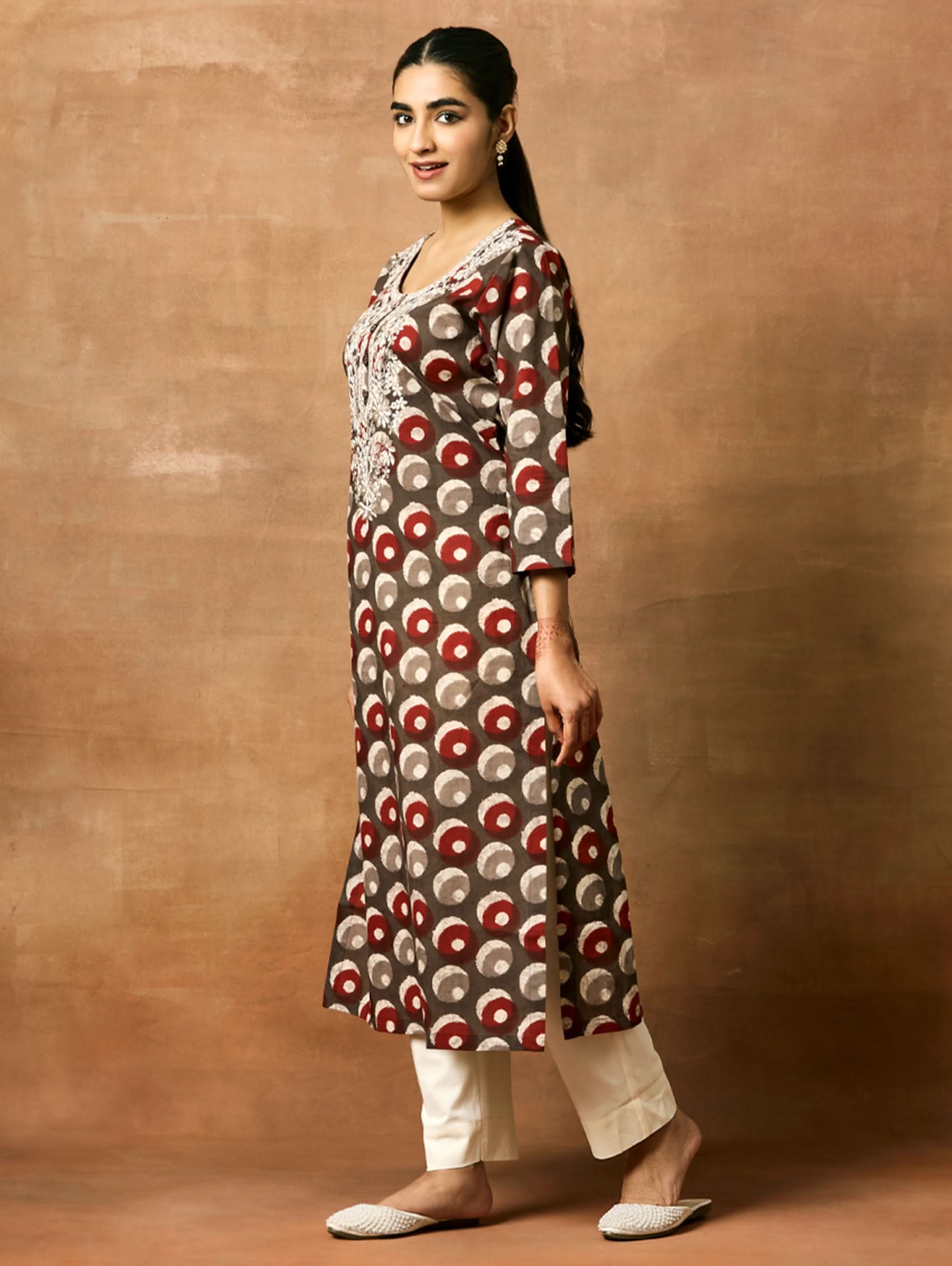 Woman wearing a patterned kurta and pants against a brown background