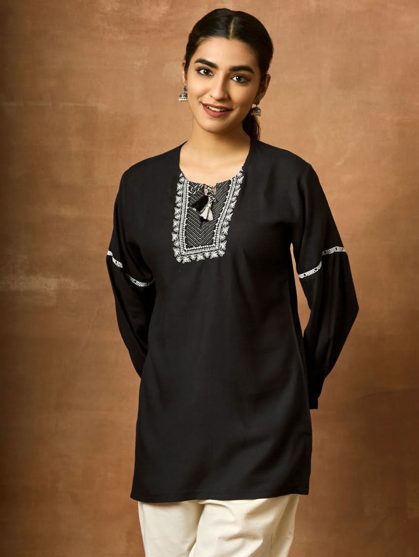 A woman wearing a black viscose rayon tunic with a round neckline, three-quarter sleeves, and computerised thread embroidery on the tunic.