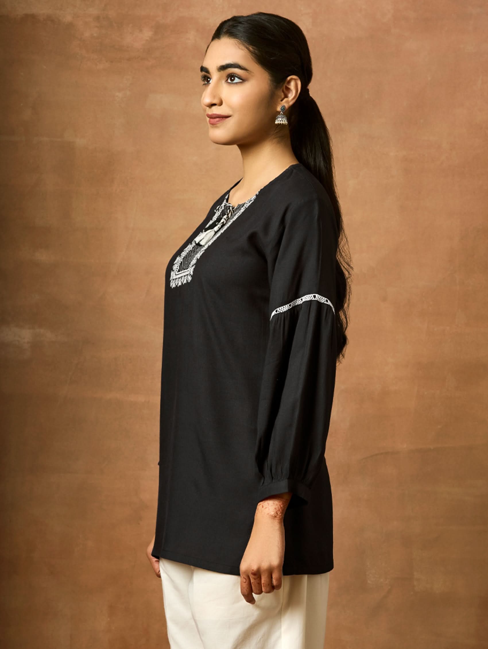 Woman wearing a black blouse with silver embroidery against a brown background