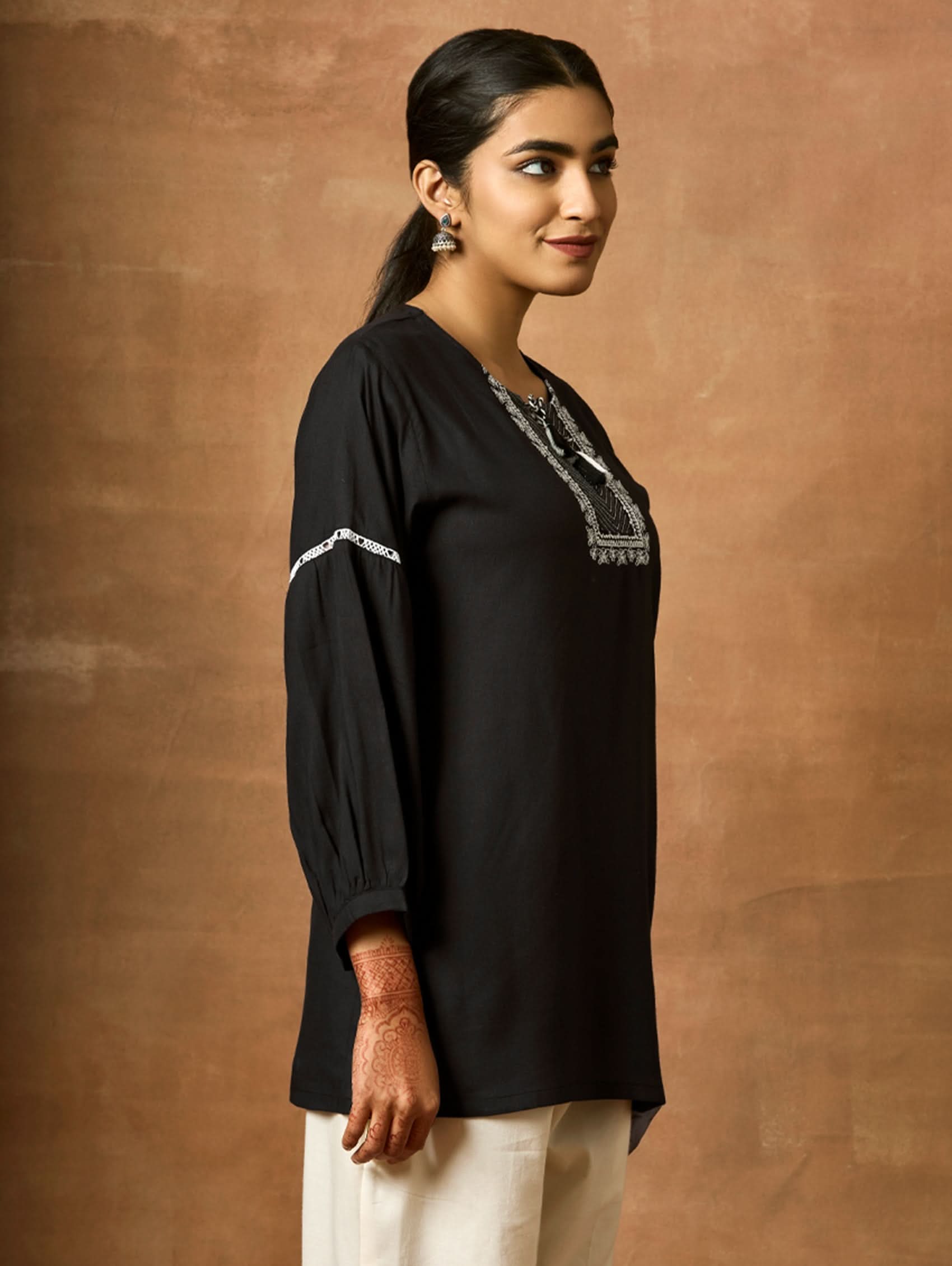 Woman wearing a black blouse with silver embroidery against a brown background