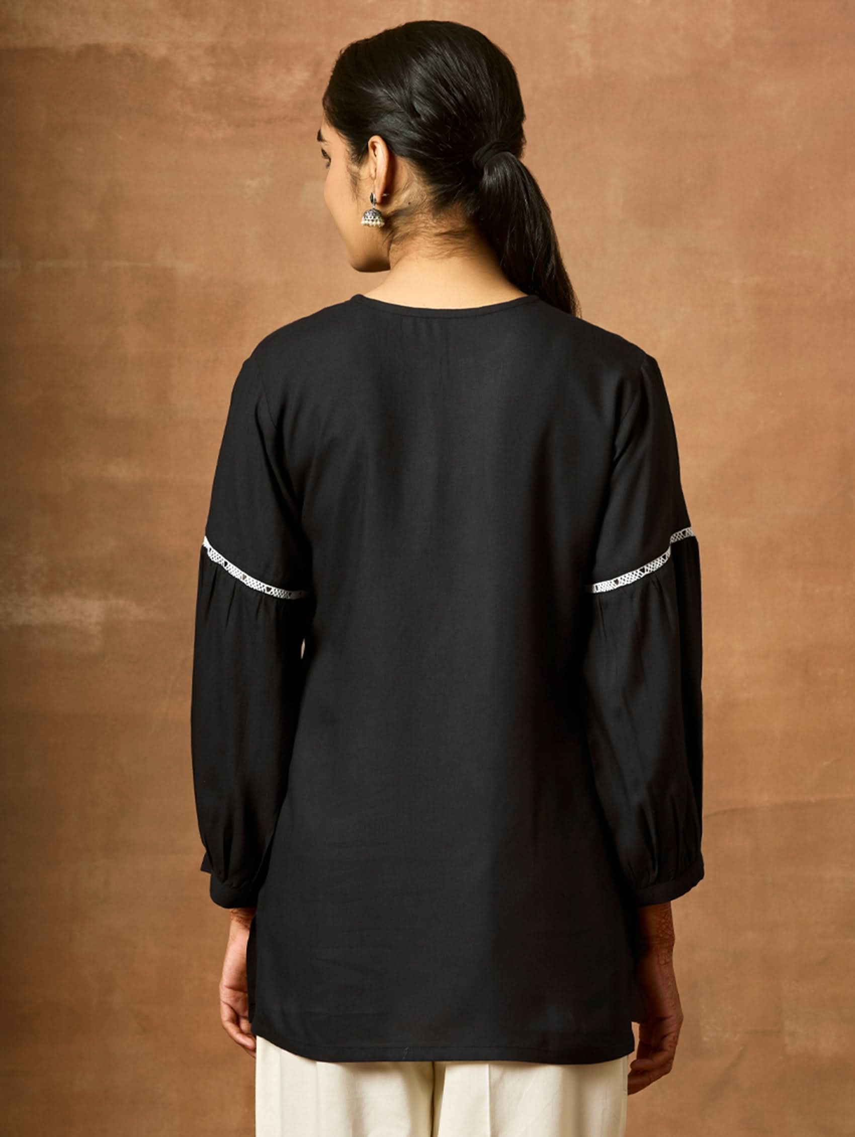 Person wearing a black top with white accents on a brown background