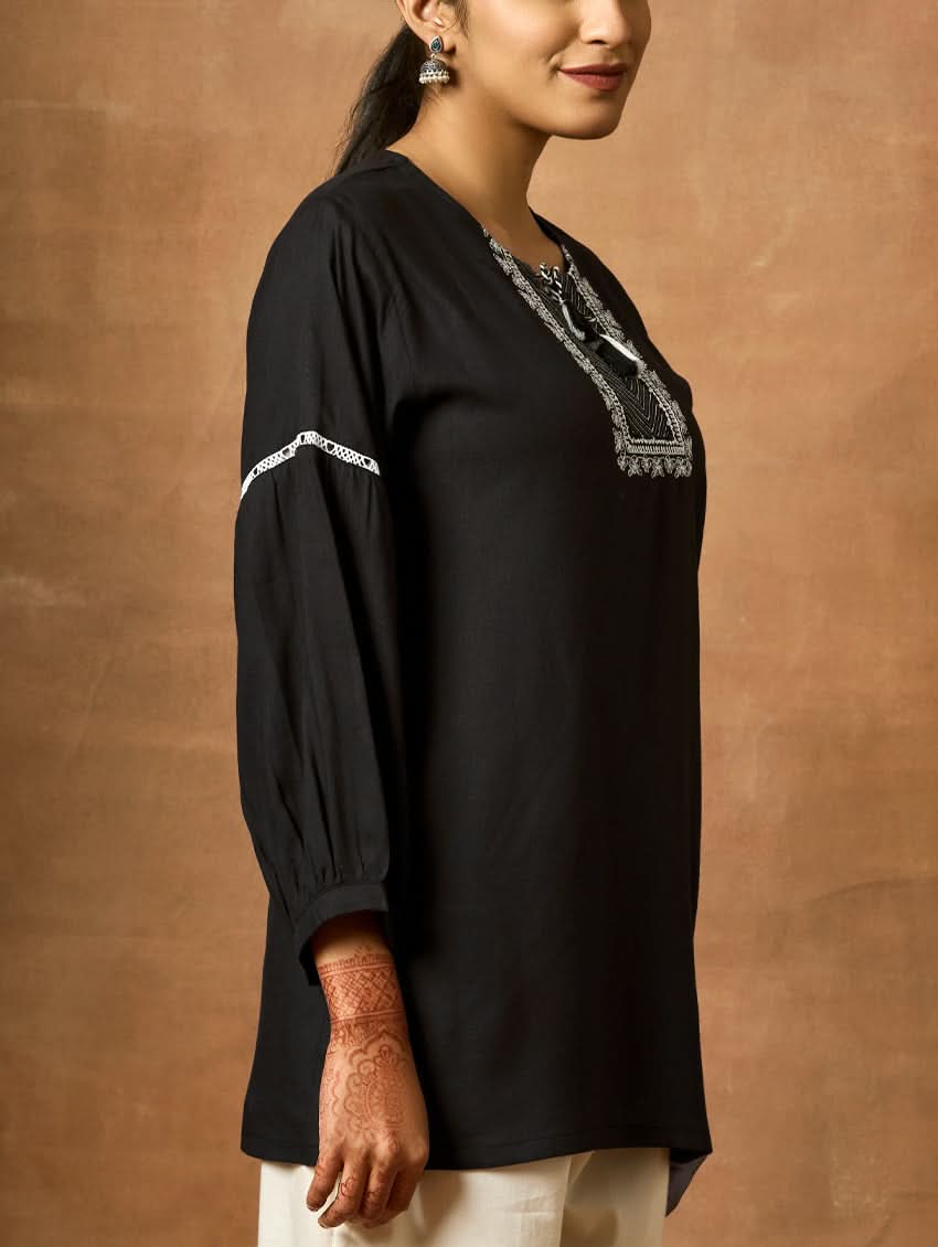 Woman wearing a black top with embroidery against a brown background