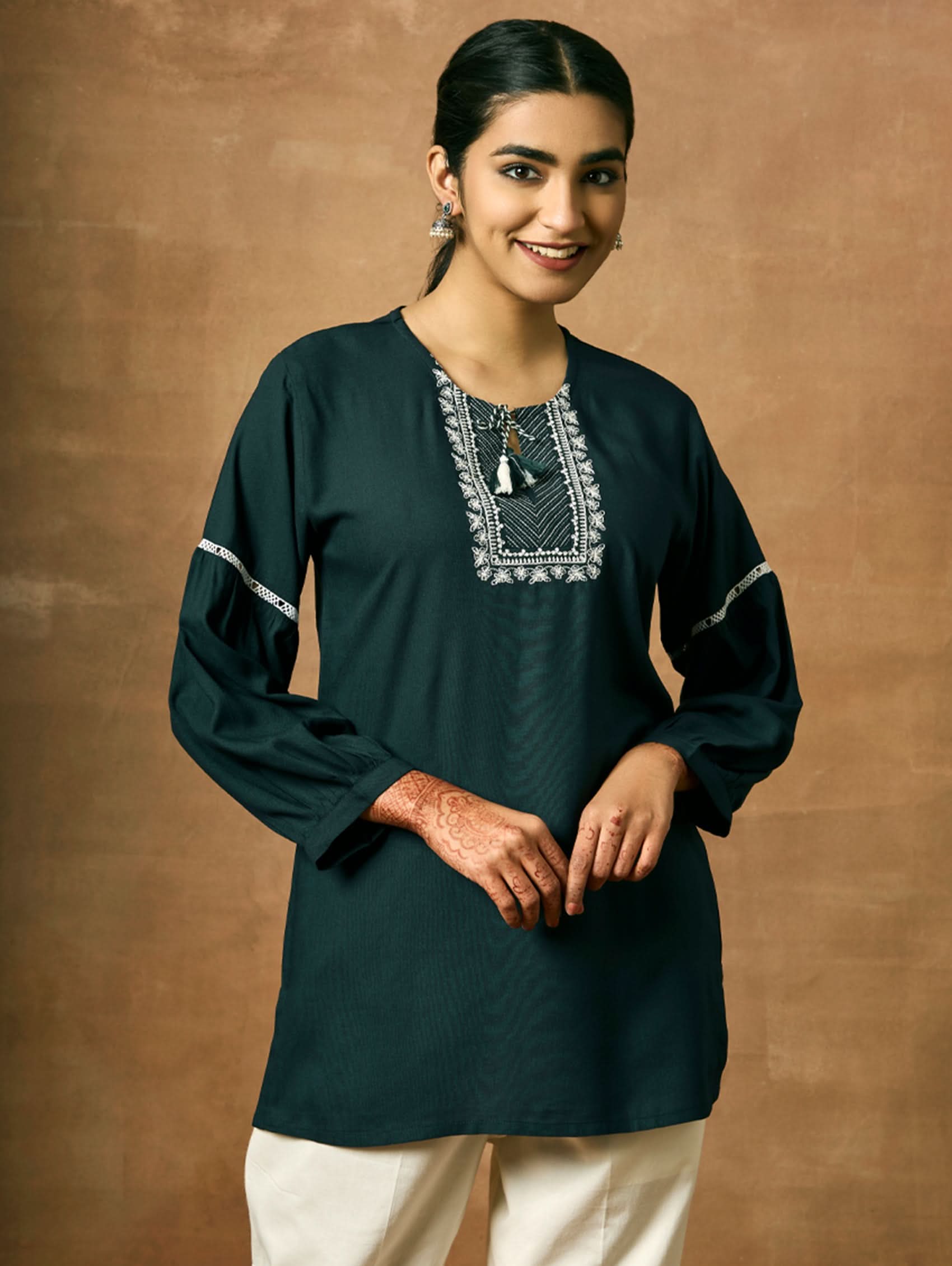 A woman wearing a black viscose rayon tunic with a round neckline, three-quarter sleeves, and computerised thread embroidery on the tunic.