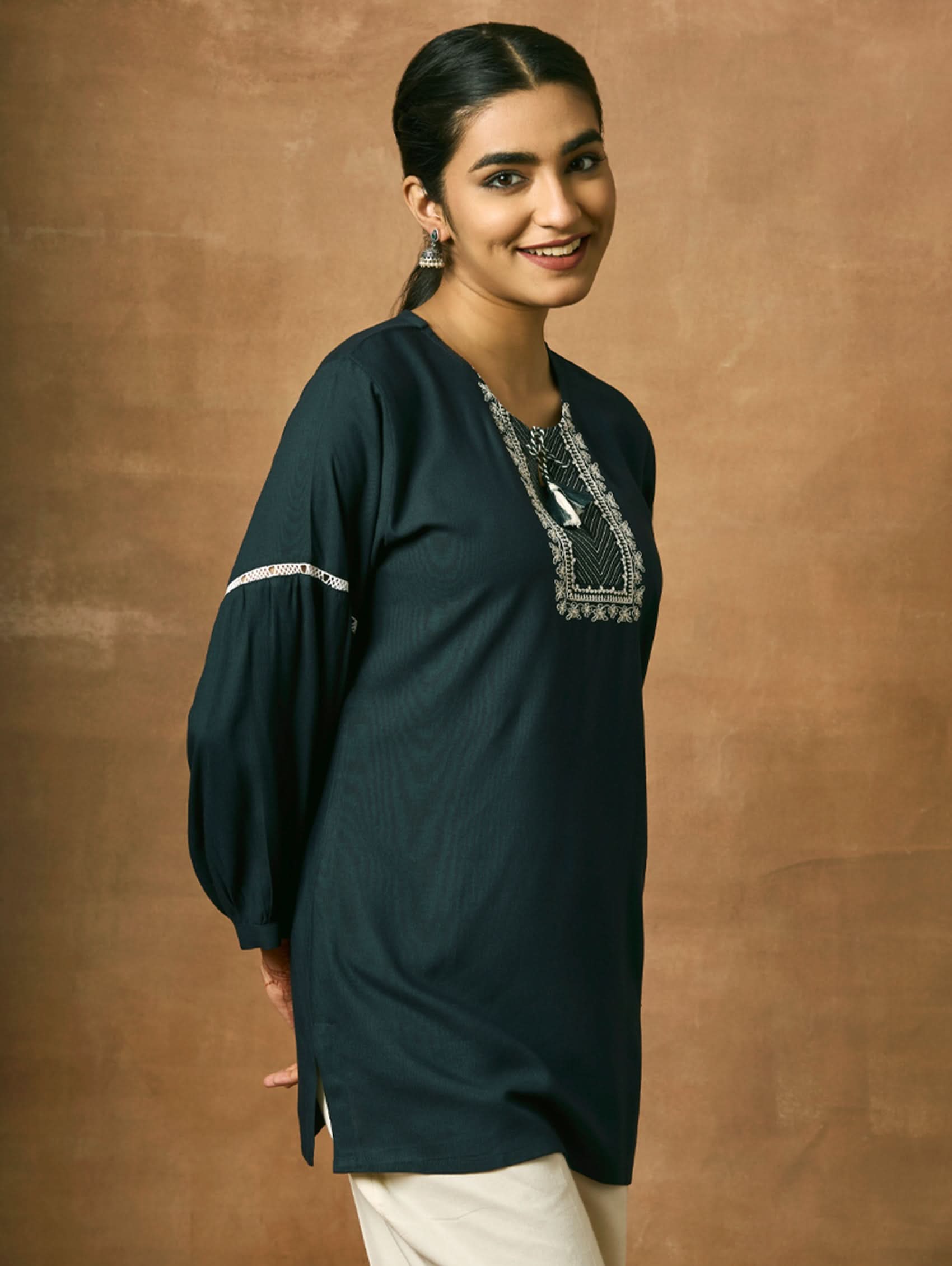 Woman wearing a black kurta with silver embroidery against a brown background.