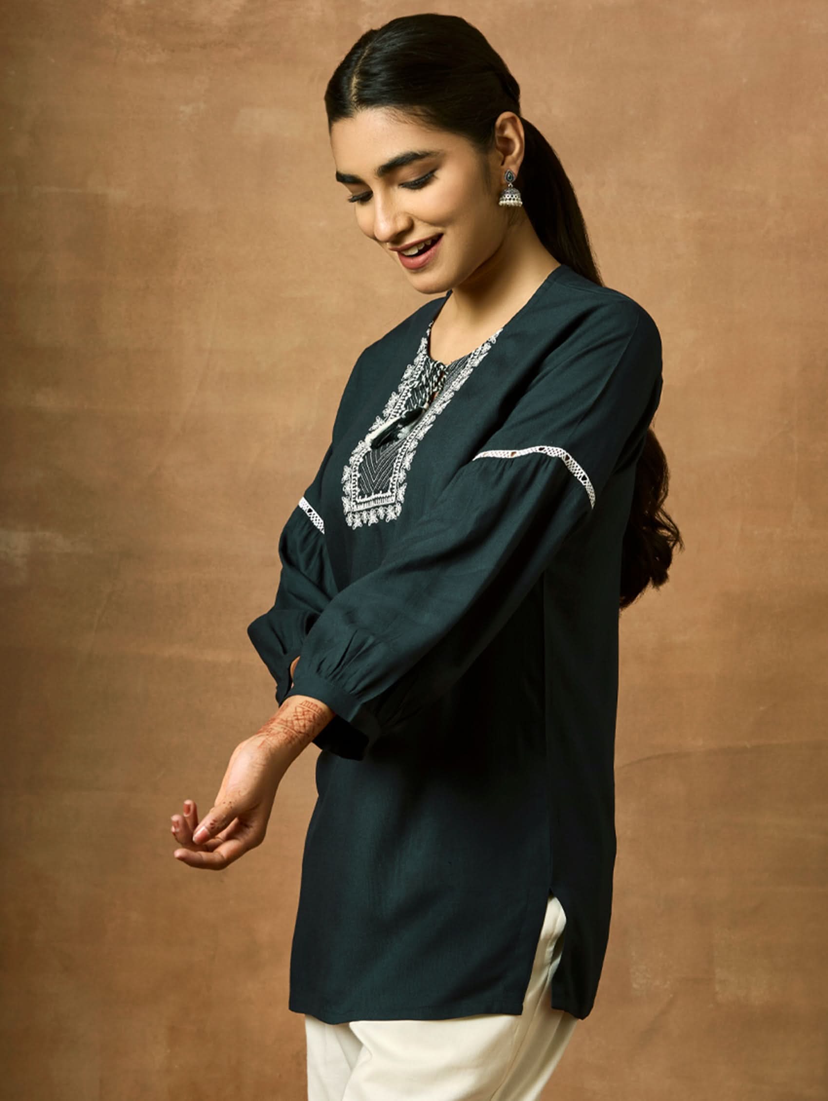 Woman wearing a dark green blouse with lace detailing against a brown background.
