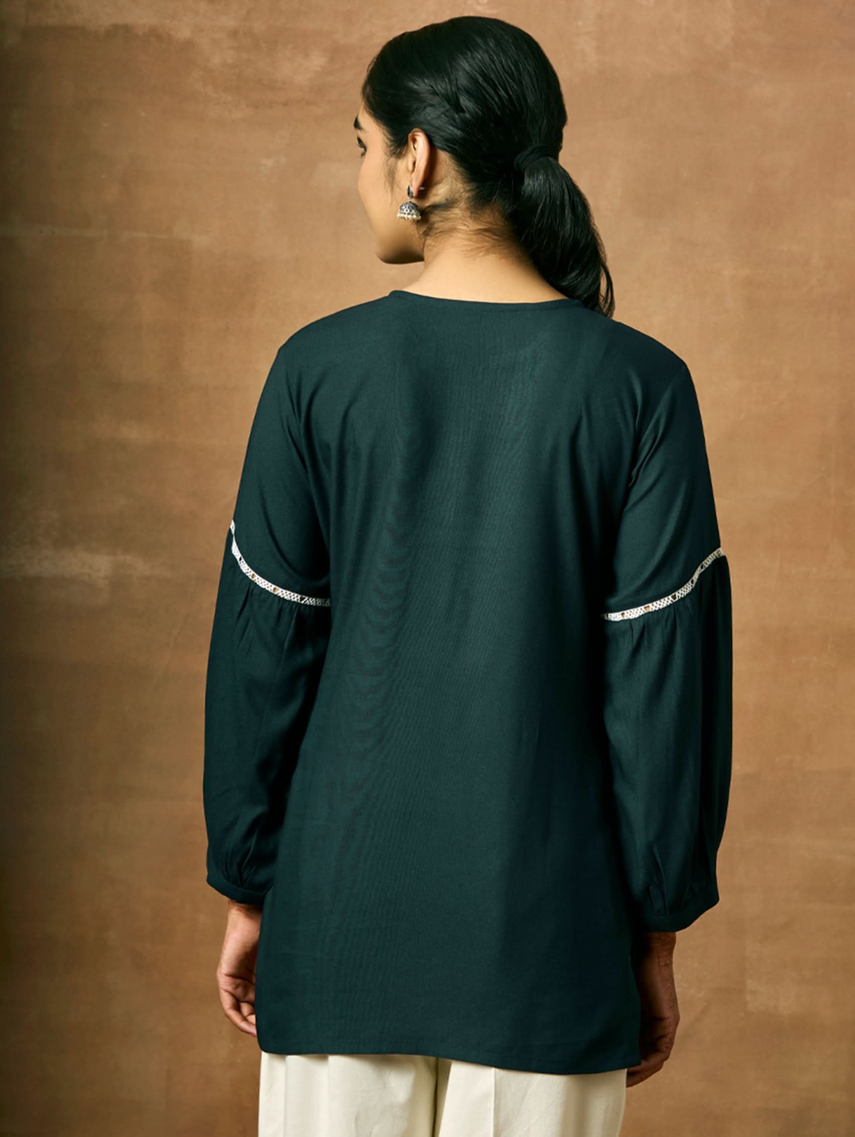 Person wearing a dark green shirt with white stripes on sleeves against a brown background.