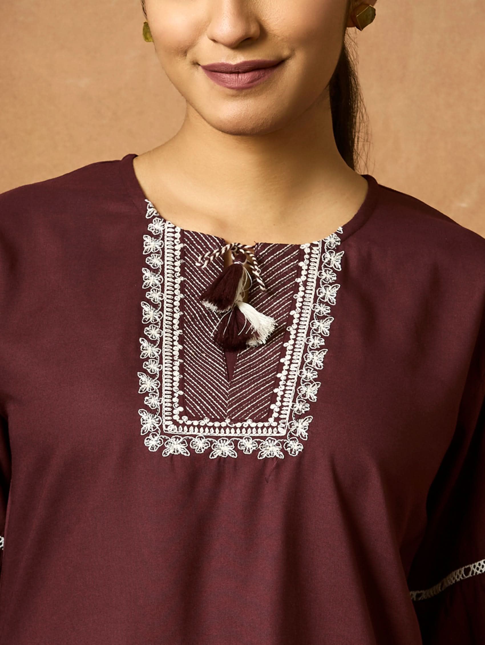 Close-up of a maroon top with lace detailing on the neckline against a neutral background.