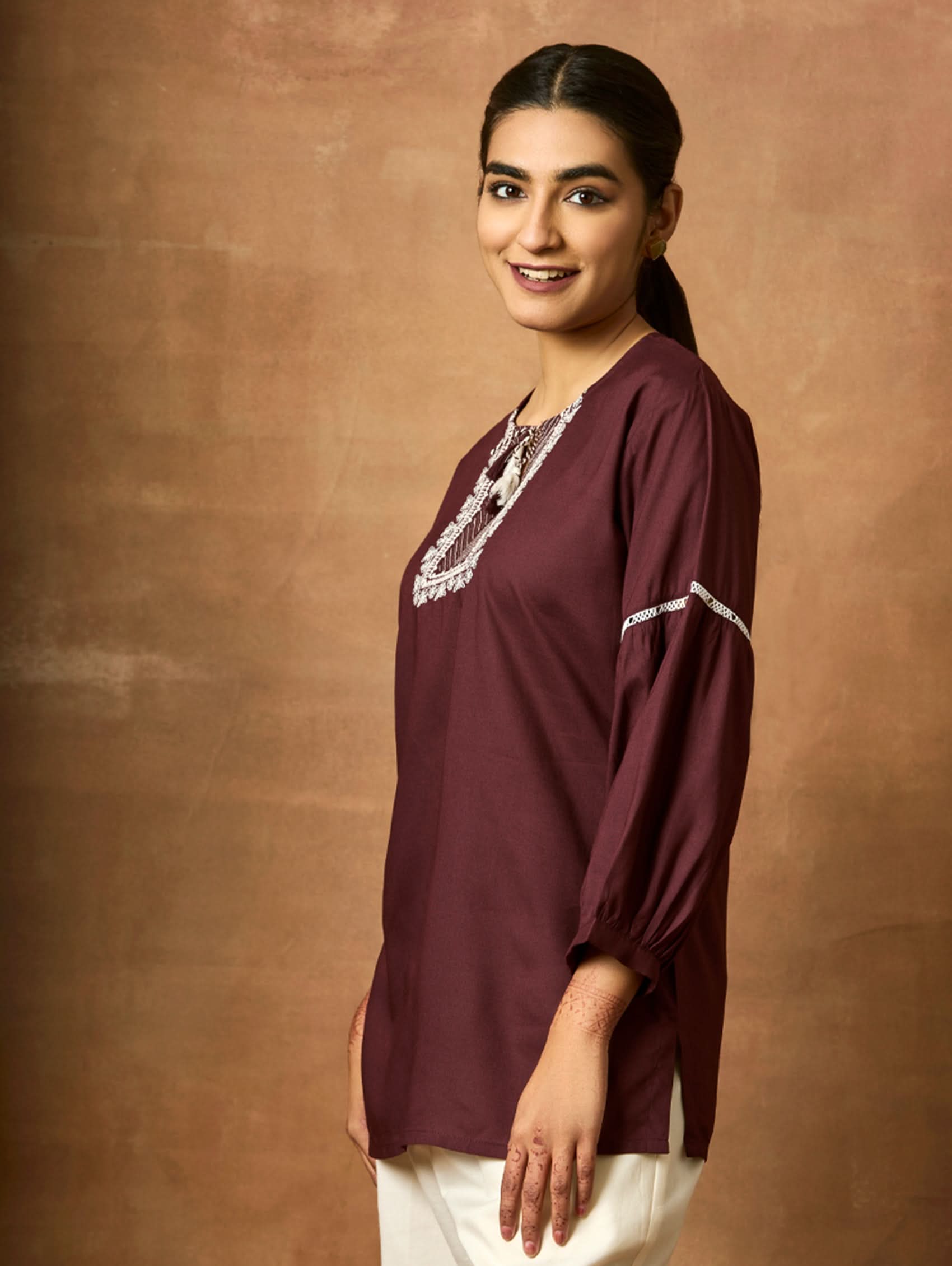 Woman wearing a maroon top with white trim against a brown background