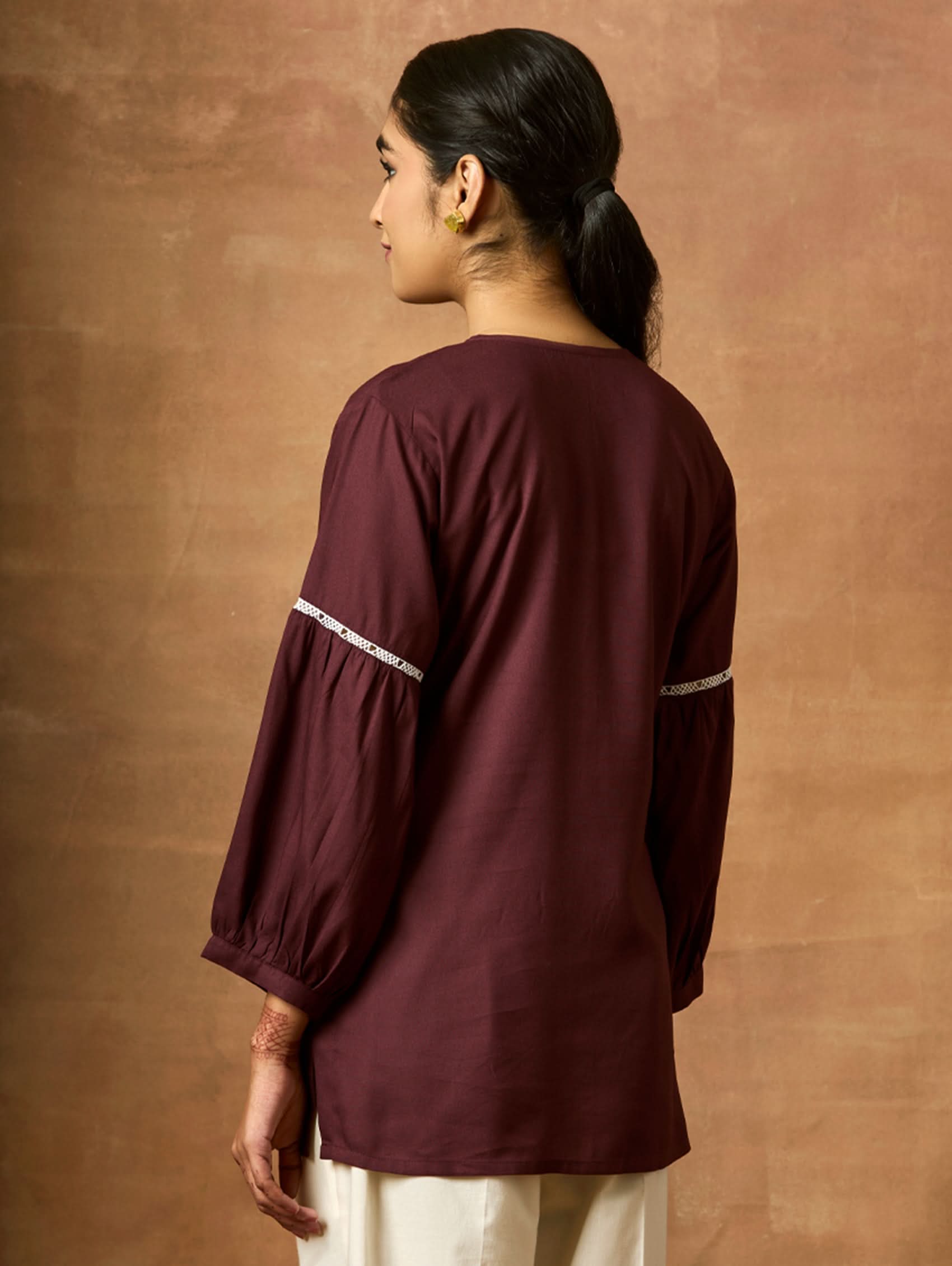 Person wearing a maroon long-sleeve top with white trim against a brown background.