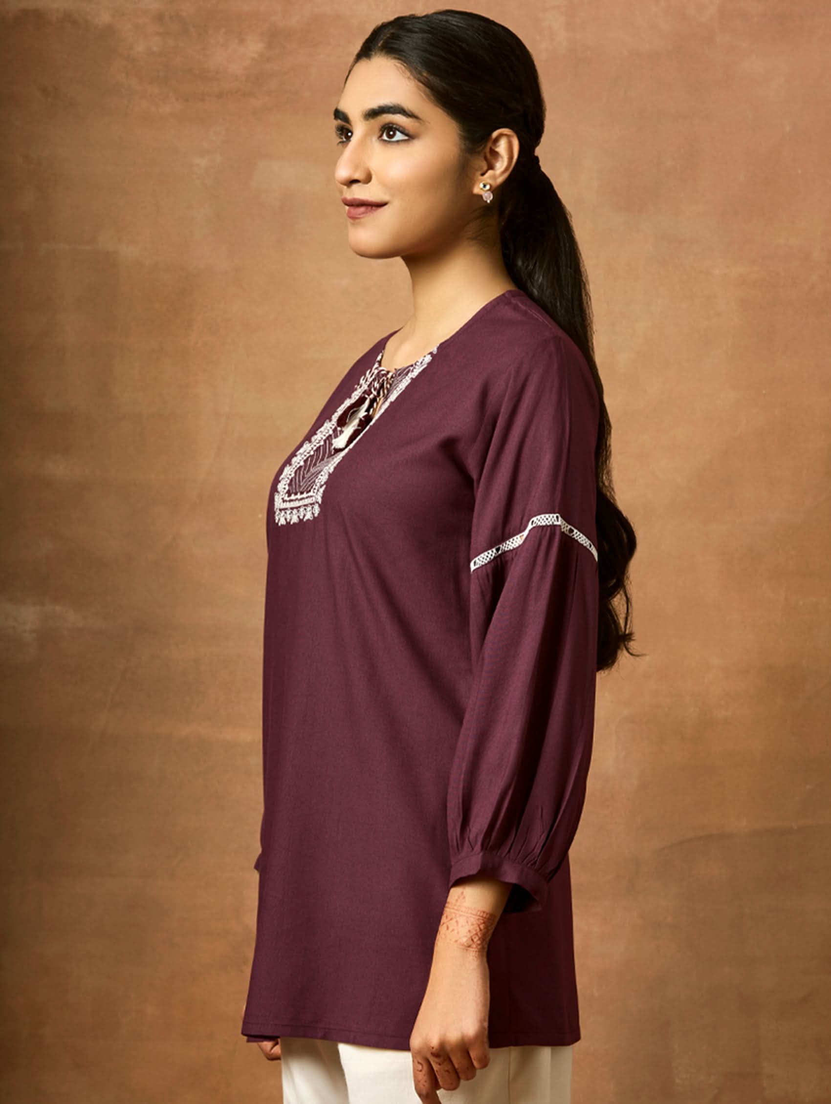 Woman wearing a purple top with lace details on a brown background