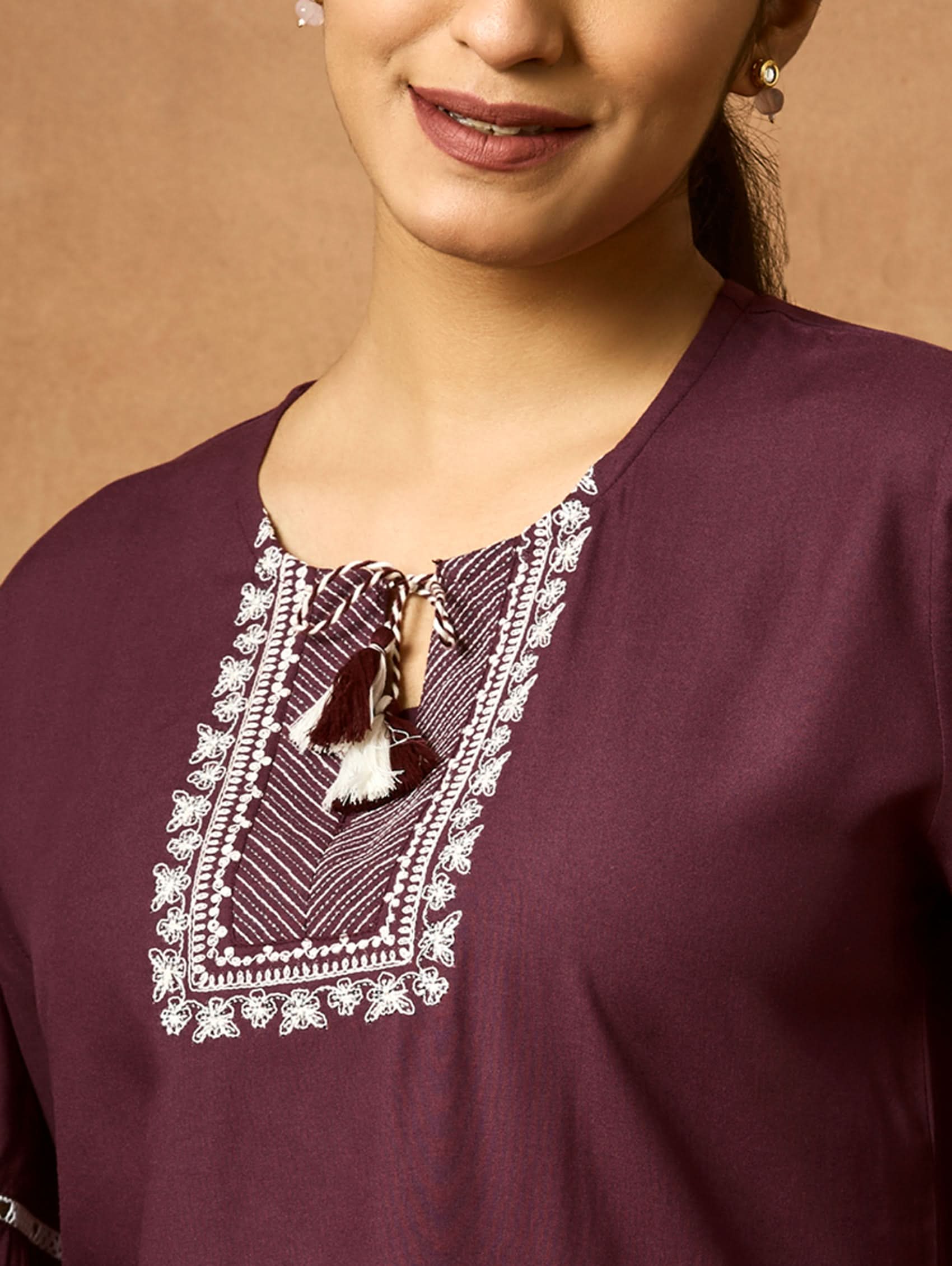 Close-up of a maroon garment with embroidered neckline against a brown background.