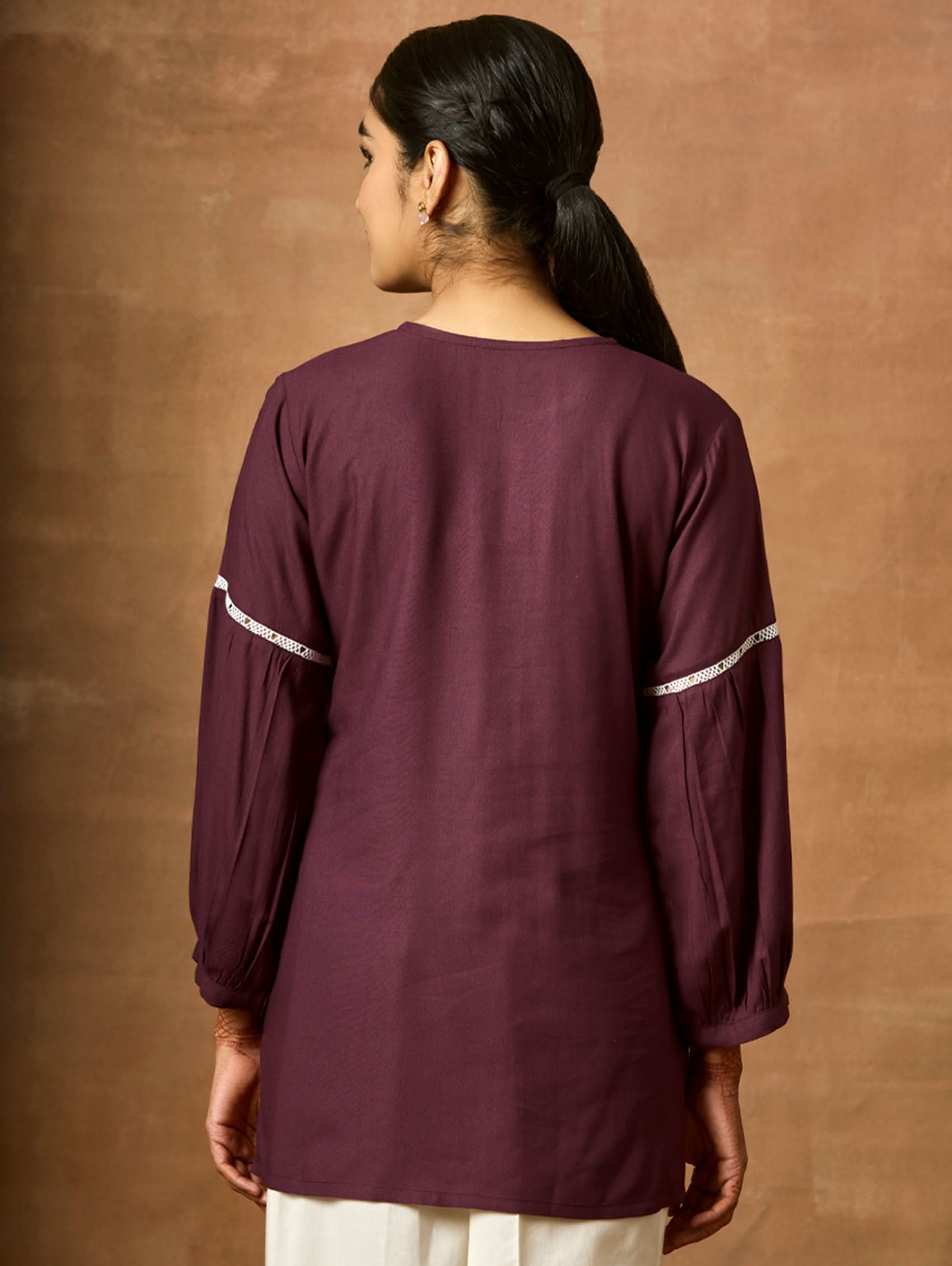 Person wearing a maroon kurta with white piping against a brown background