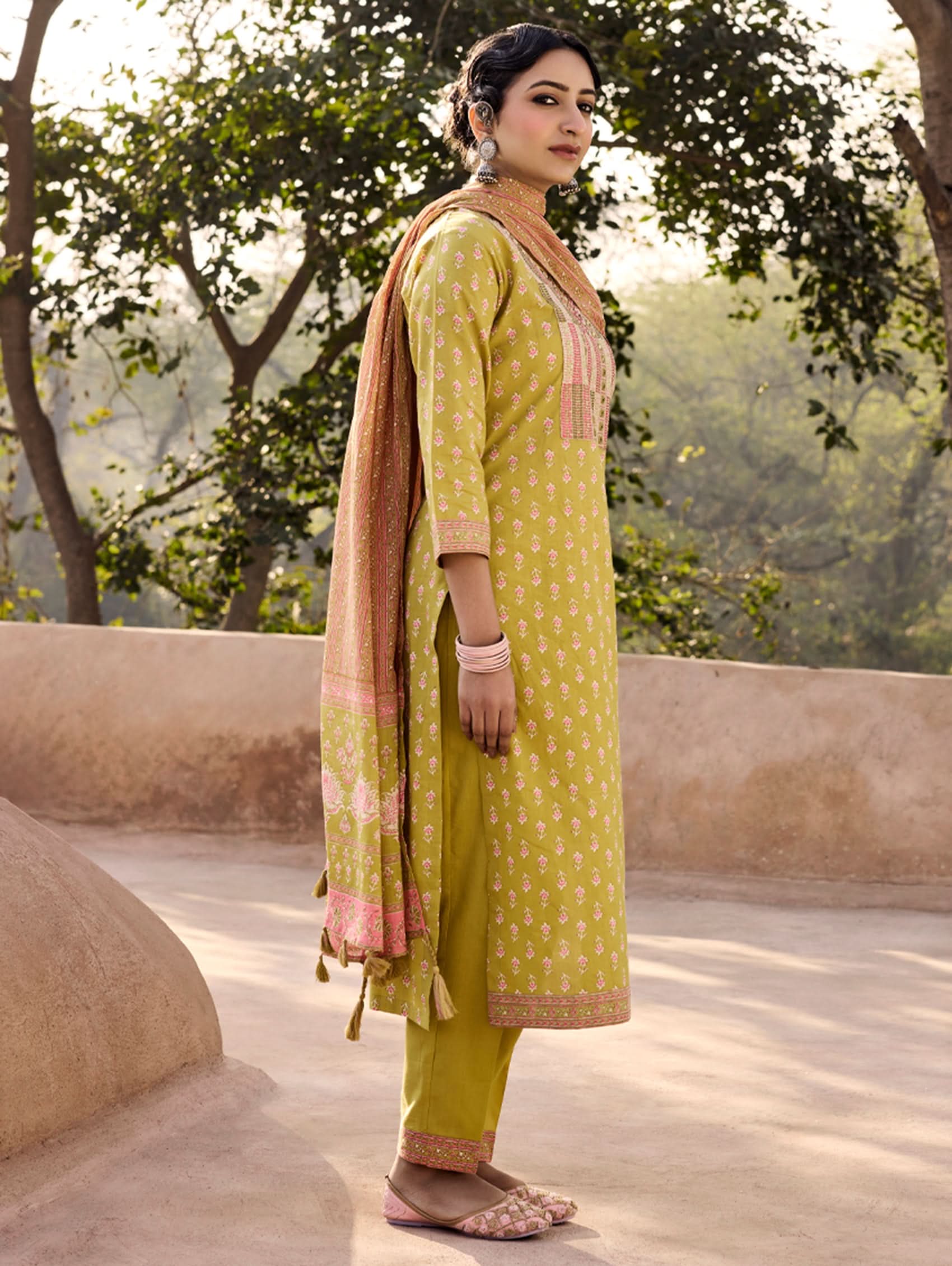 A woman wearing a green and orange cotton suit set with embroidery, consisting of a kurta with pants and a dupatta.