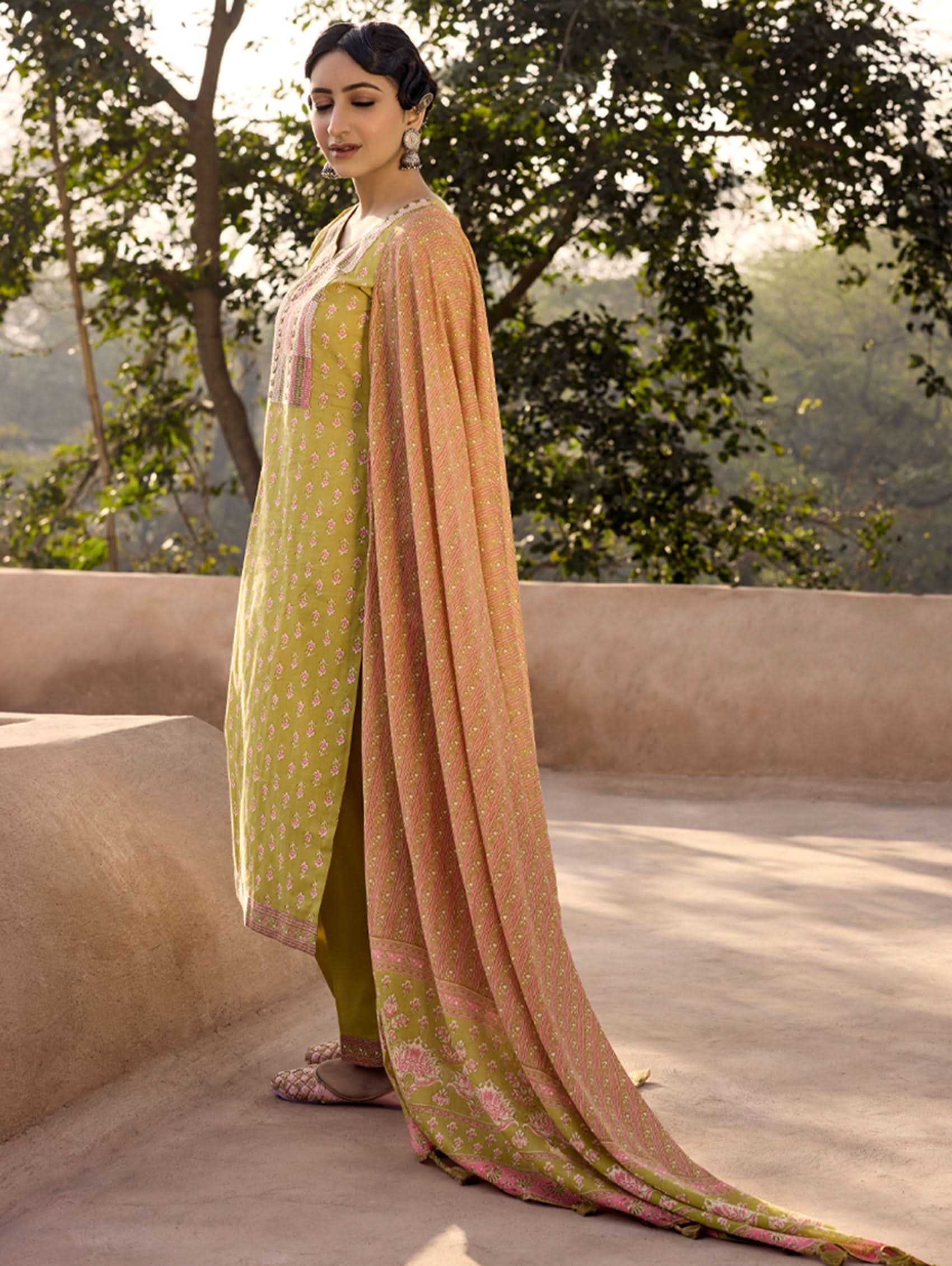 A woman wearing a green and orange cotton suit set with embroidery, consisting of a kurta with pants and a dupatta.