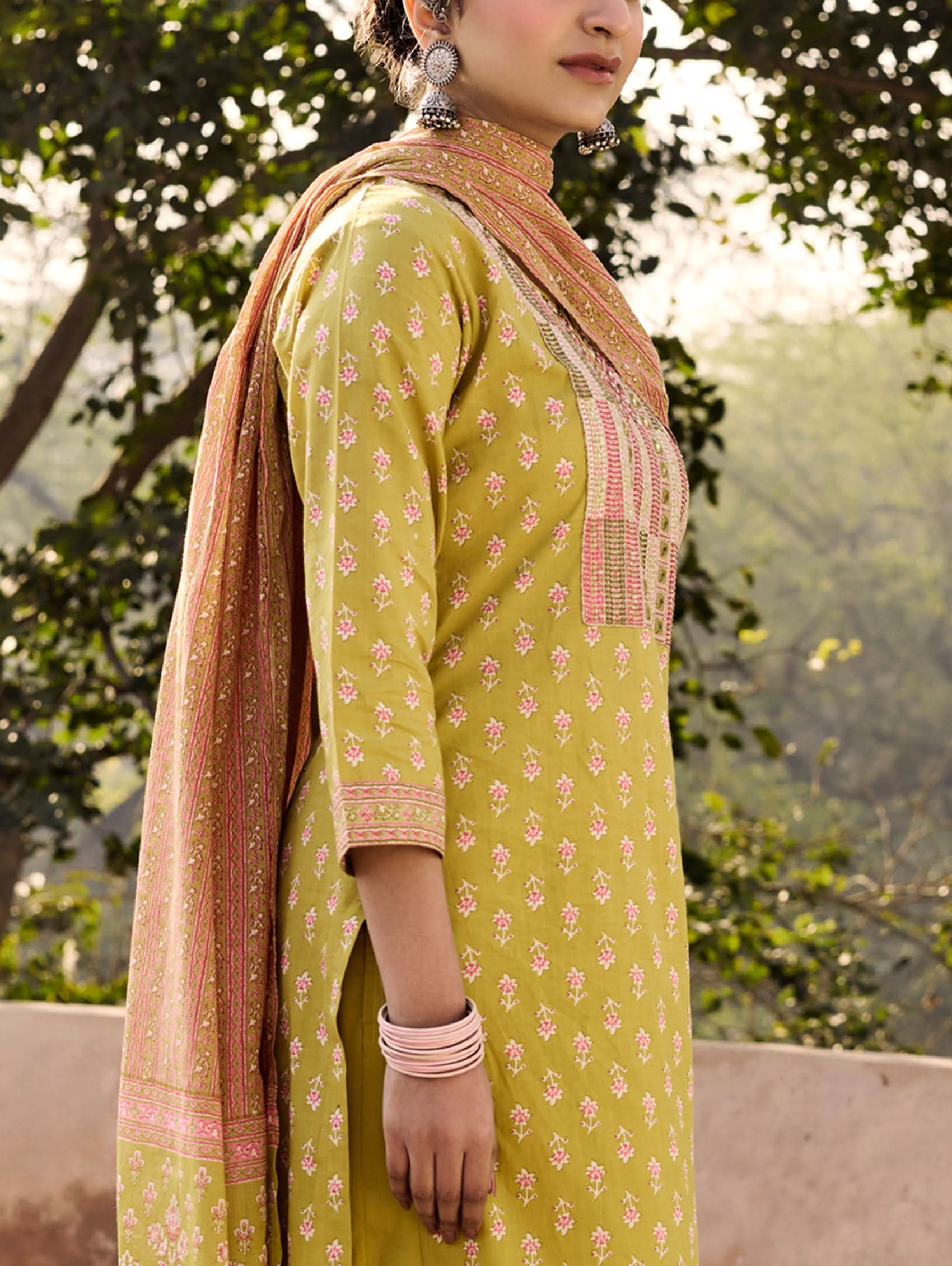 A woman wearing a green and orange cotton suit set with embroidery, consisting of a kurta with pants and a dupatta.