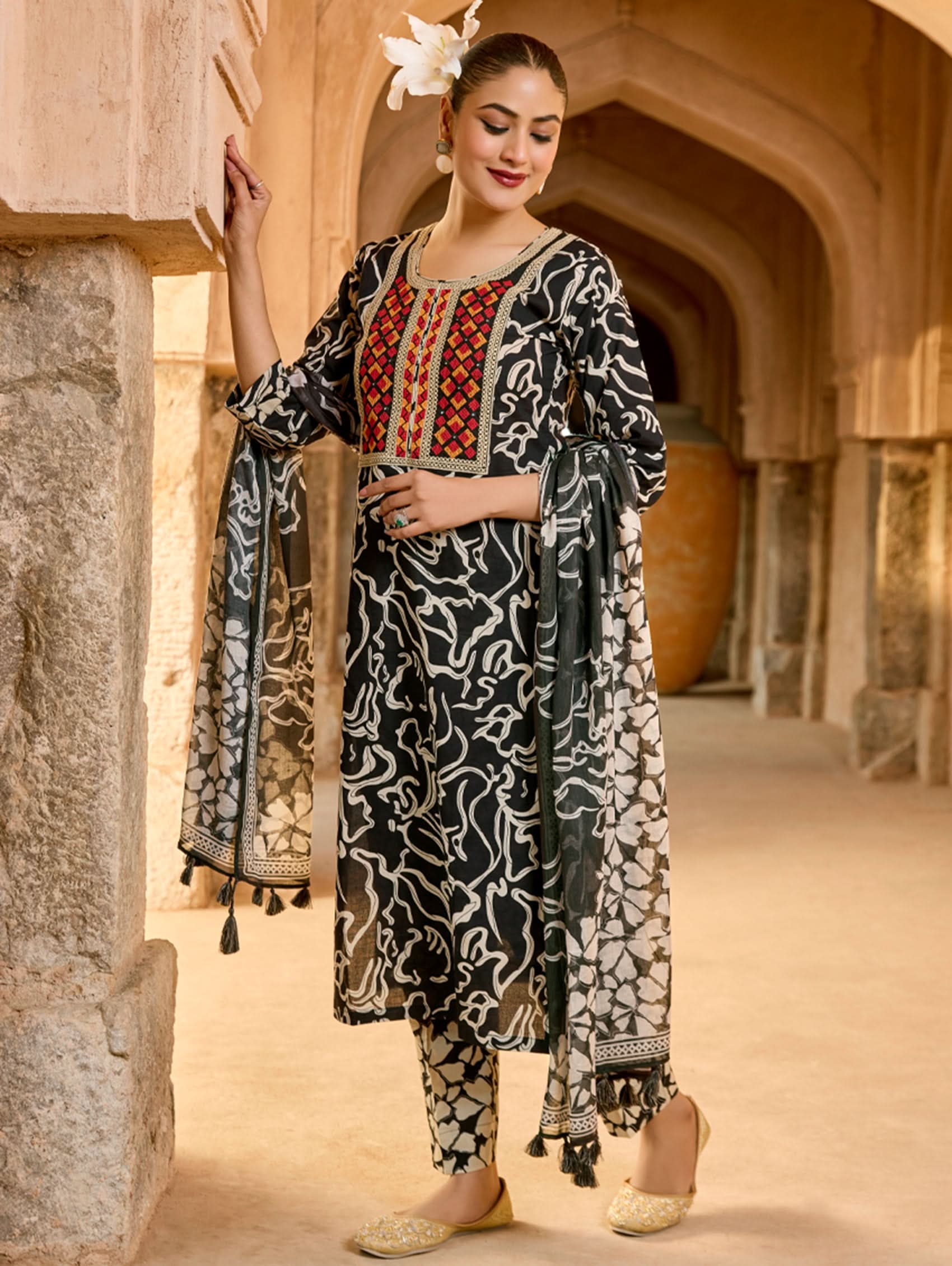 A woman wearing a traditional cotton suit set with embroidery and a digitally printed dupatta, standing in an archway.
