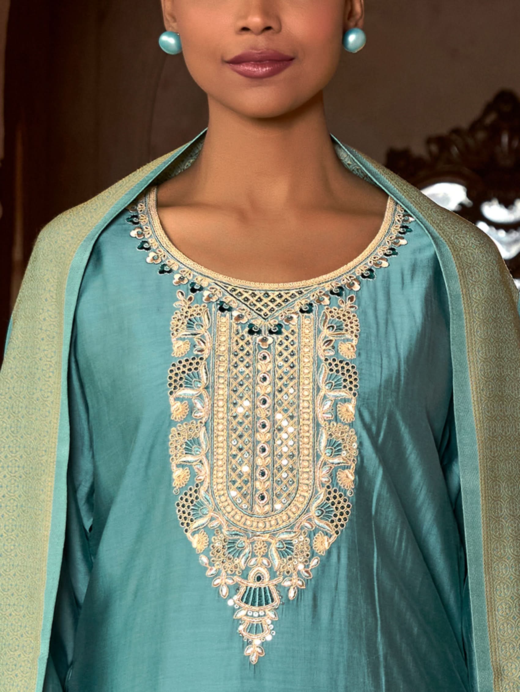 A woman wearing a blue viscose silk suit set with embroidered details, consisting of a kurta, pants, and a dupatta, standing in front of a pot.