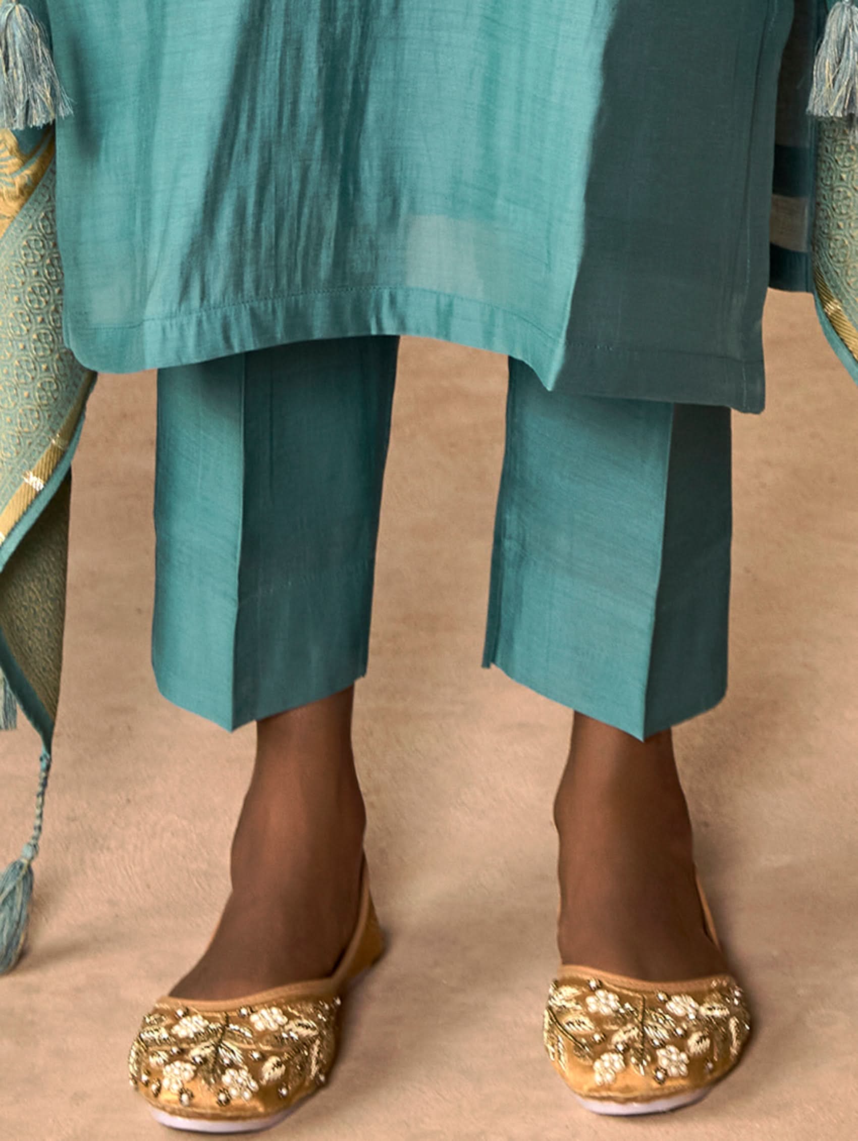 A woman wearing a blue viscose silk suit set with embroidered details, consisting of a kurta, pants, and a dupatta, standing in front of a pot.