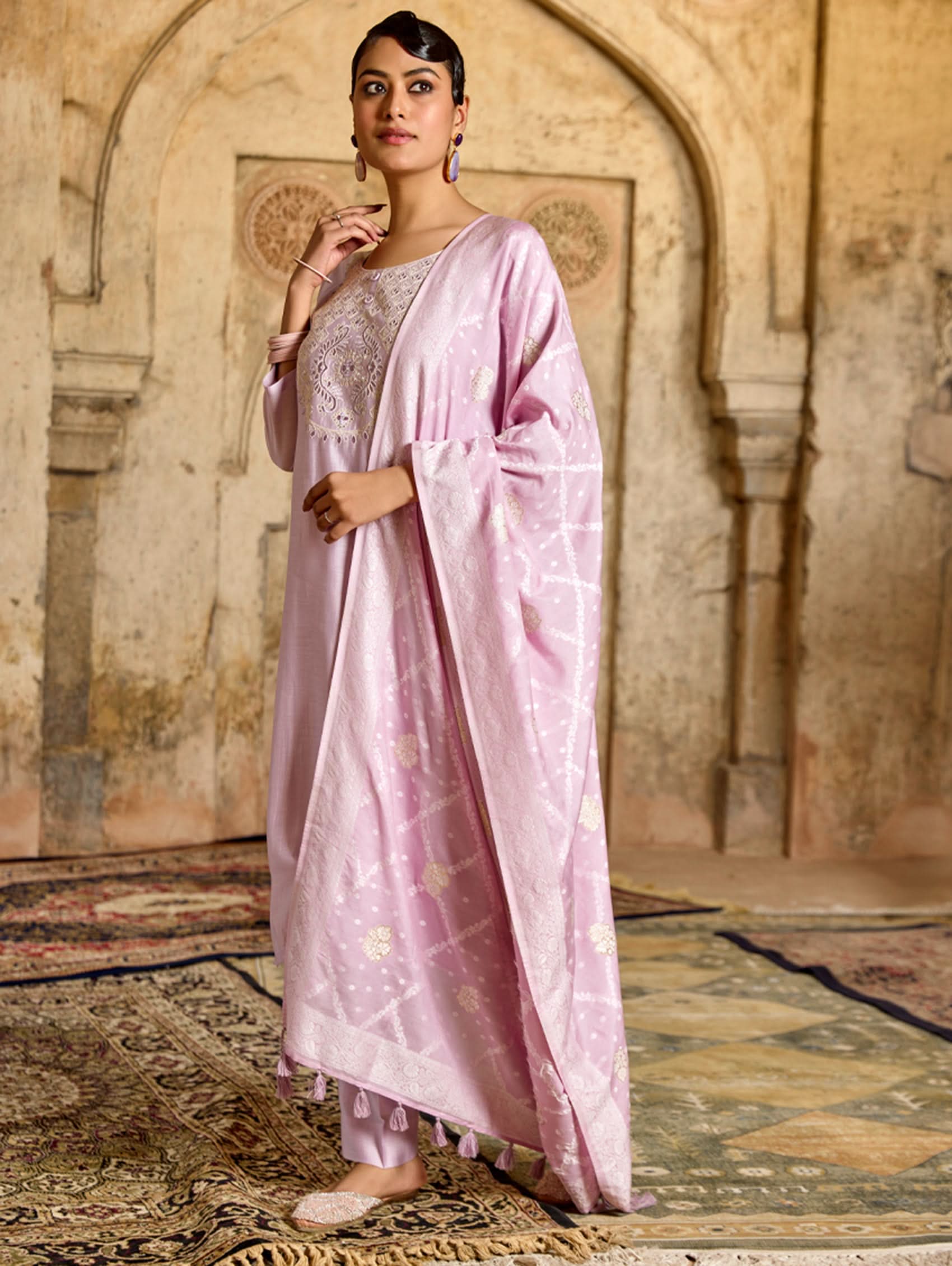 A woman modeling a pink viscose silk suit set with embroidered details, consisting of a kurta, pants, and a jacquard weave silk dupatta.