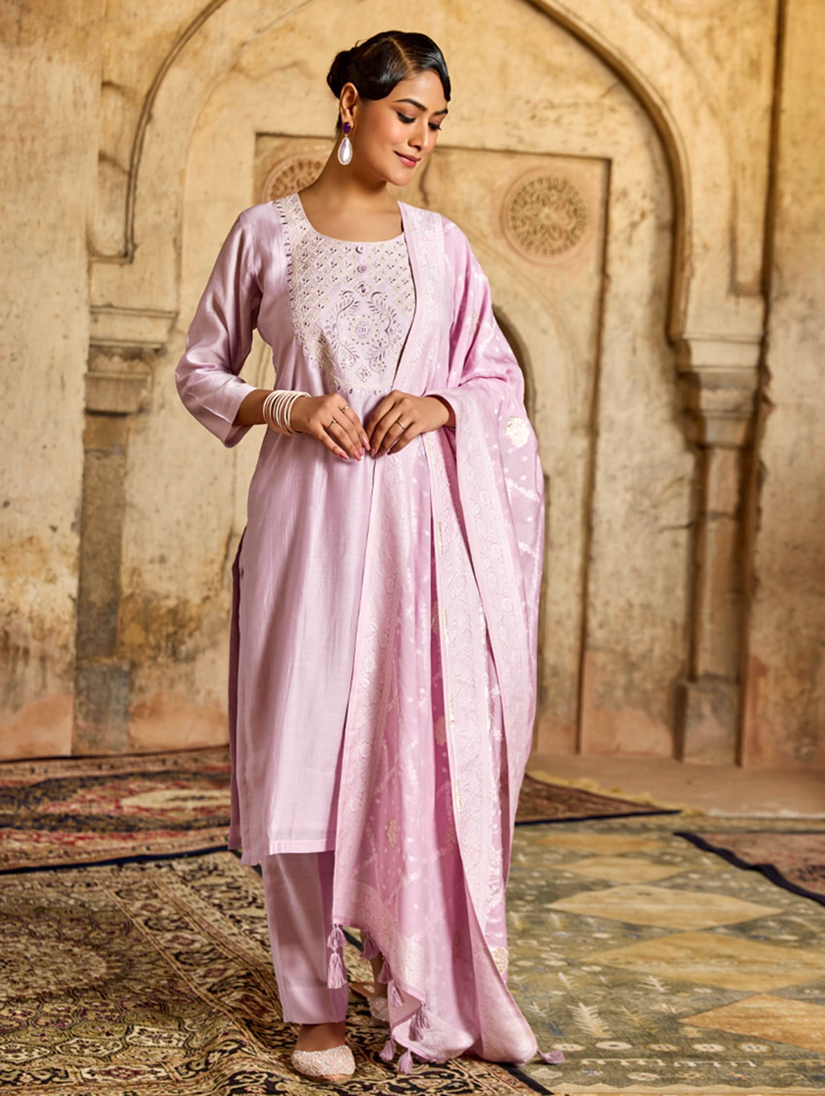 A woman wearing a pink viscose silk suit set with embroidered details, consisting of a kurta, pants, and a jacquard weave silk dupatta.