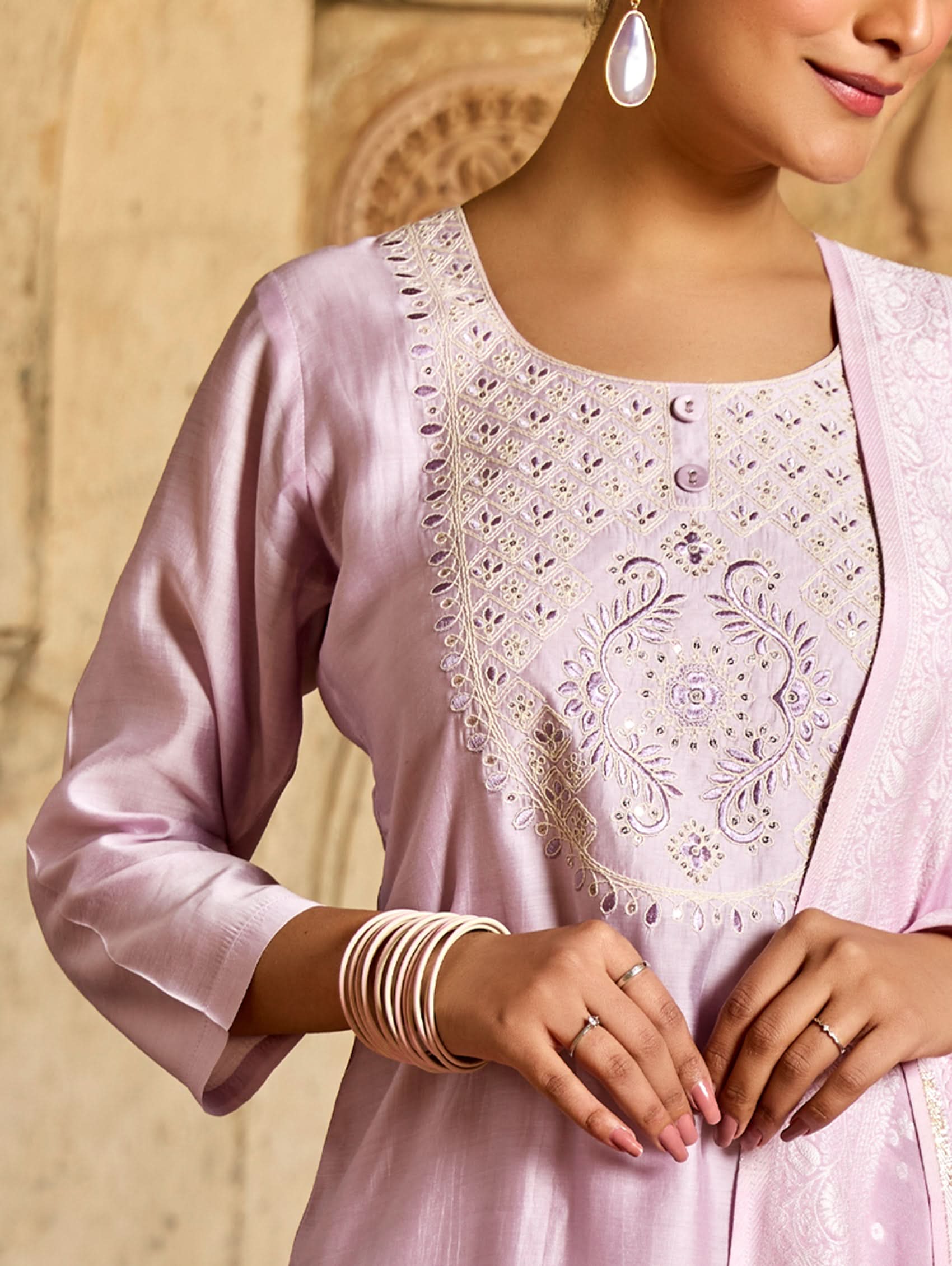 A woman wearing a pink viscose silk suit set with embroidered details, consisting of a kurta, pants, and a jacquard weave silk dupatta.