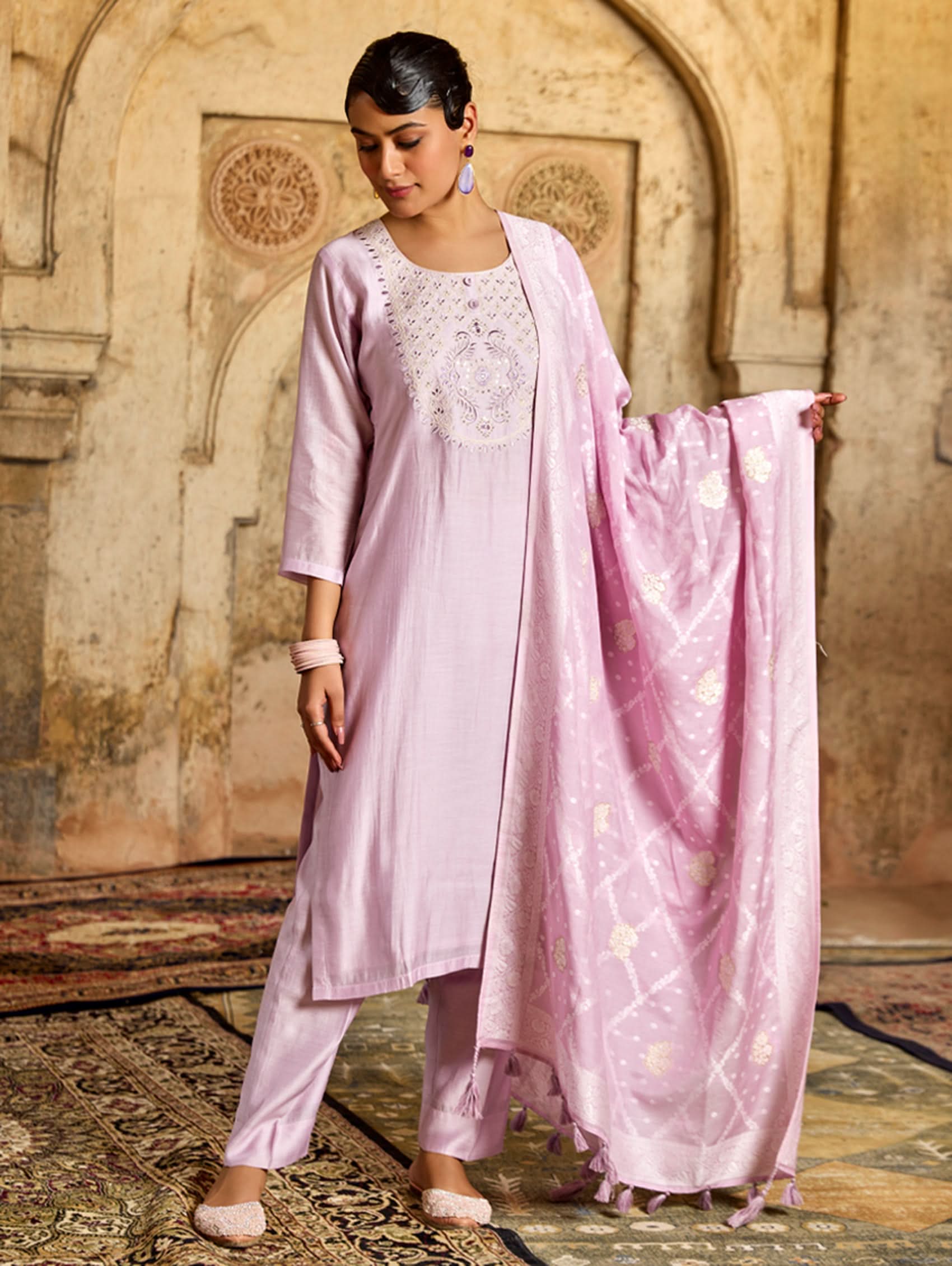 A woman wearing a pink viscose silk suit set with embroidered details, consisting of a kurta, pants, and a jacquard weave silk dupatta.