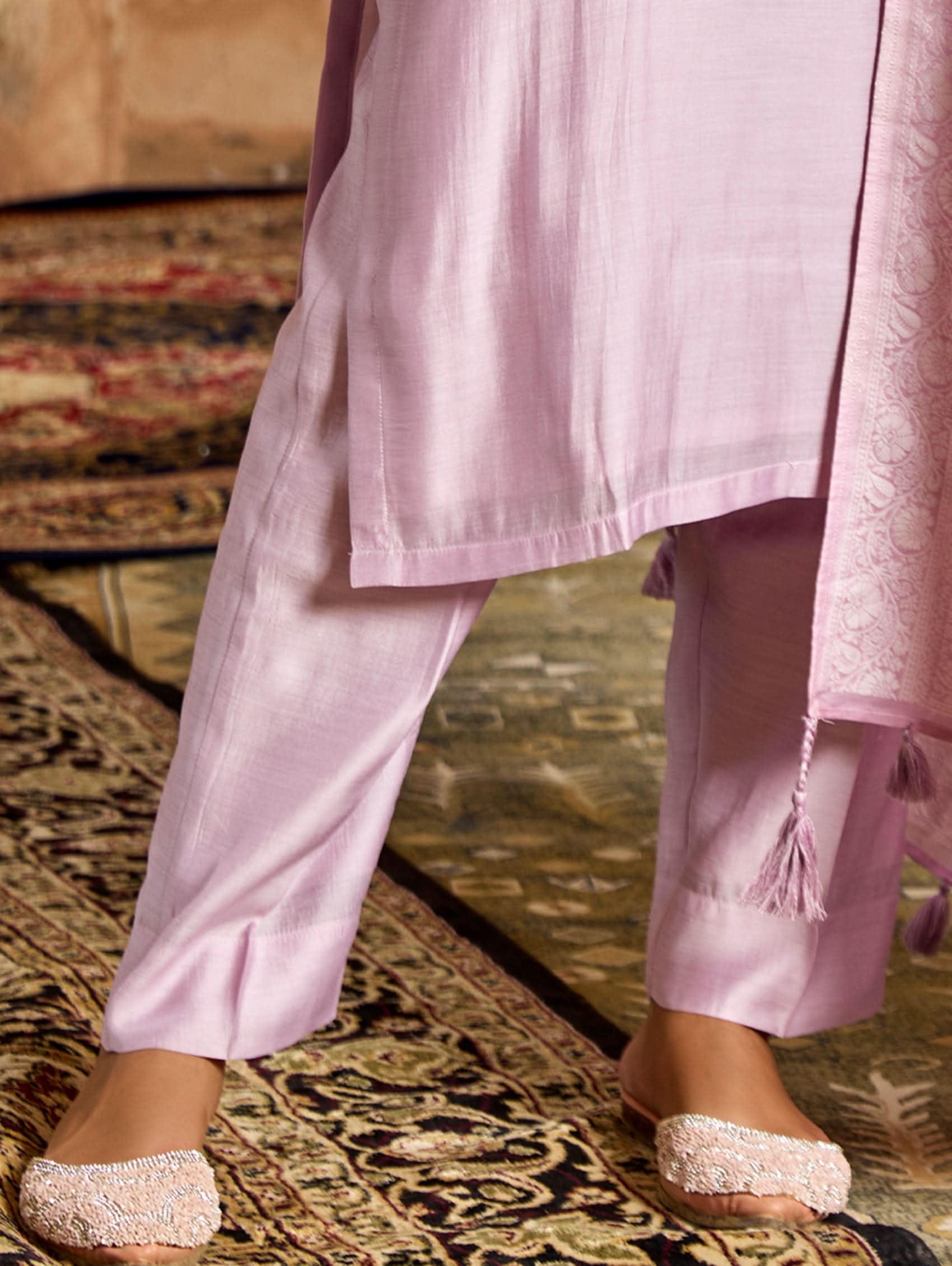 A woman wearing a pink viscose silk suit set with embroidered details, consisting of a kurta, pants, and a jacquard weave silk dupatta.